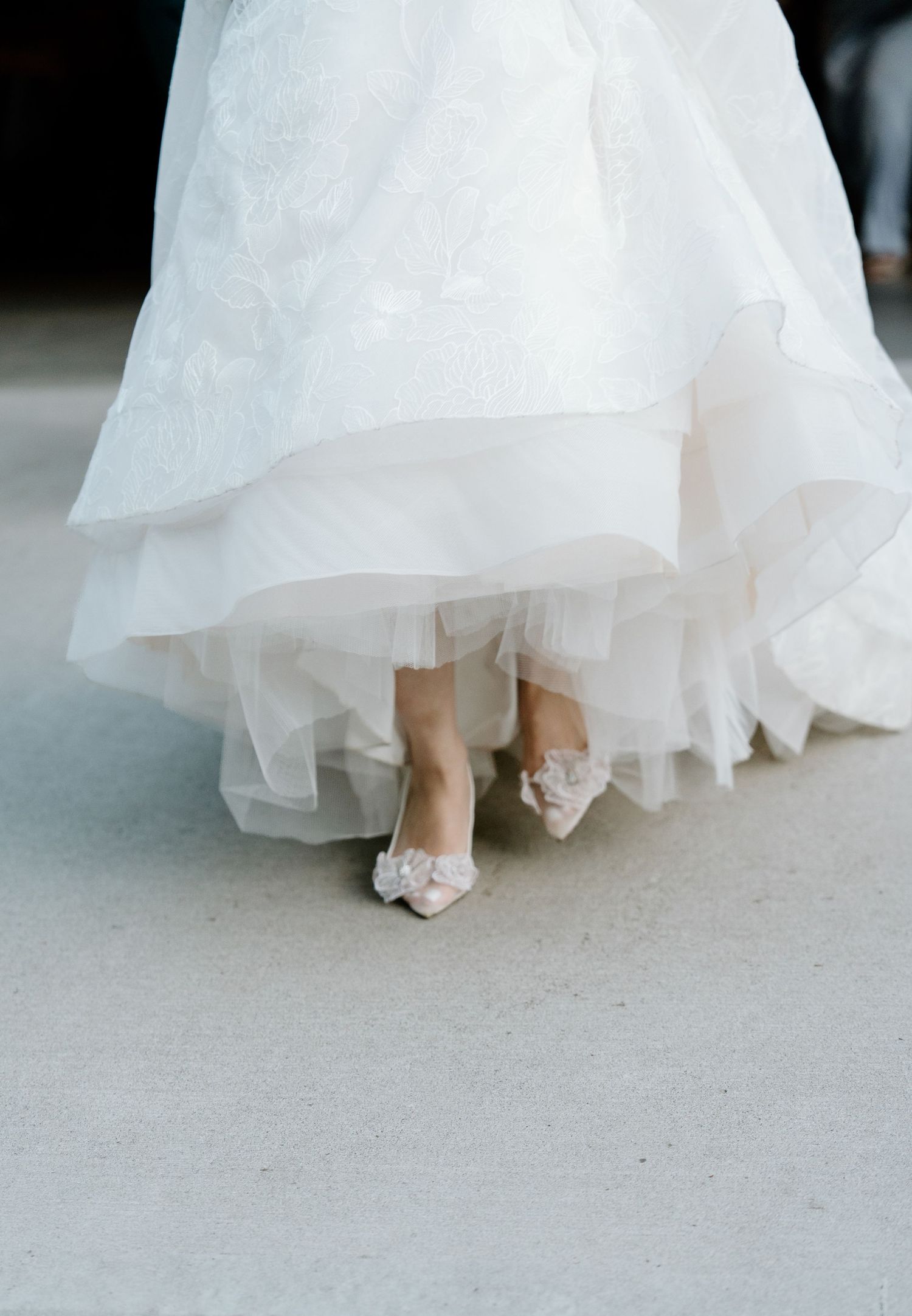 Close-up sequence showing delicate white wedding dress hem and elegant bridal shoes on concrete floor.