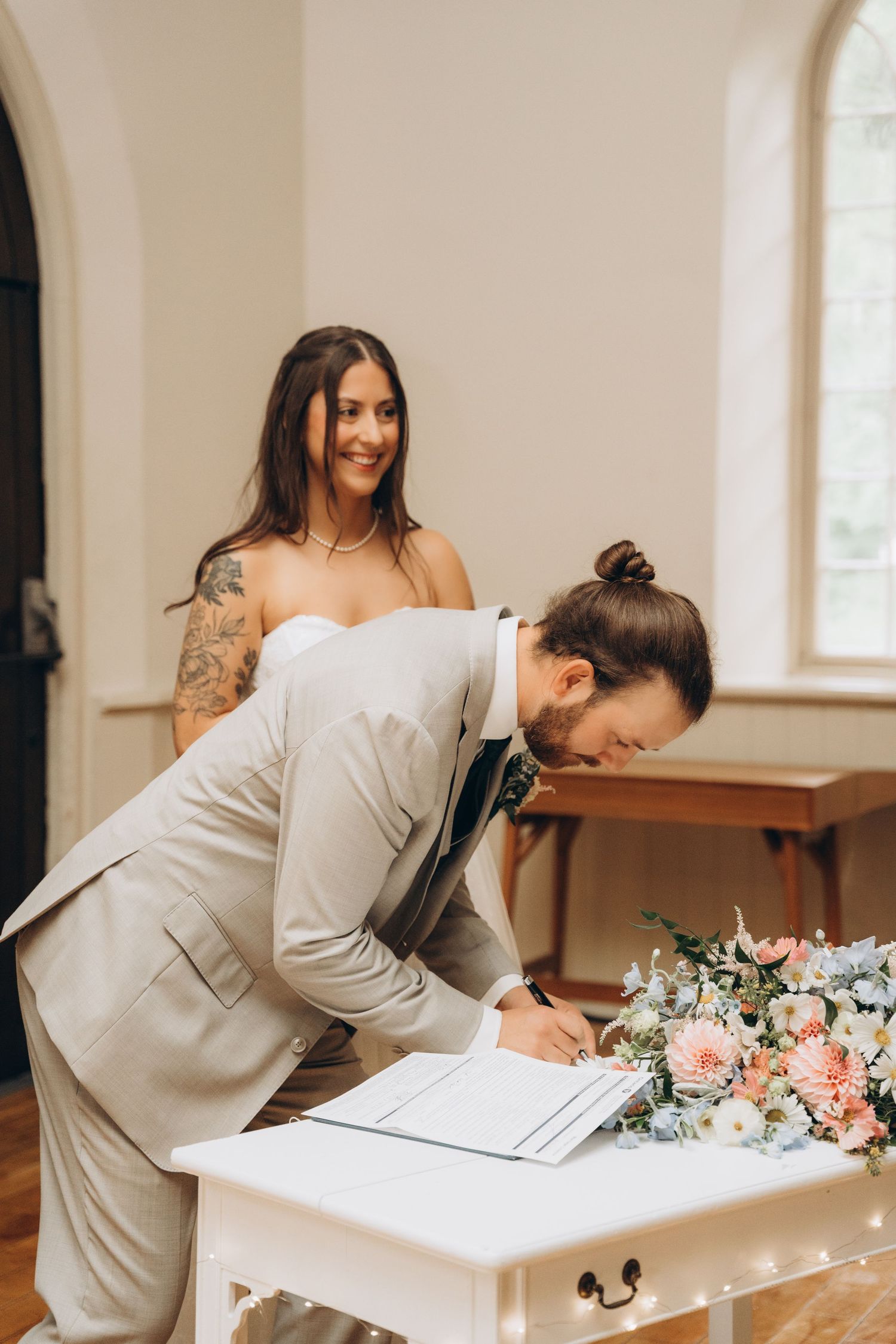 A sequence of four photos showing someone signing a document at a white desk with pink floral arrangements nearby.