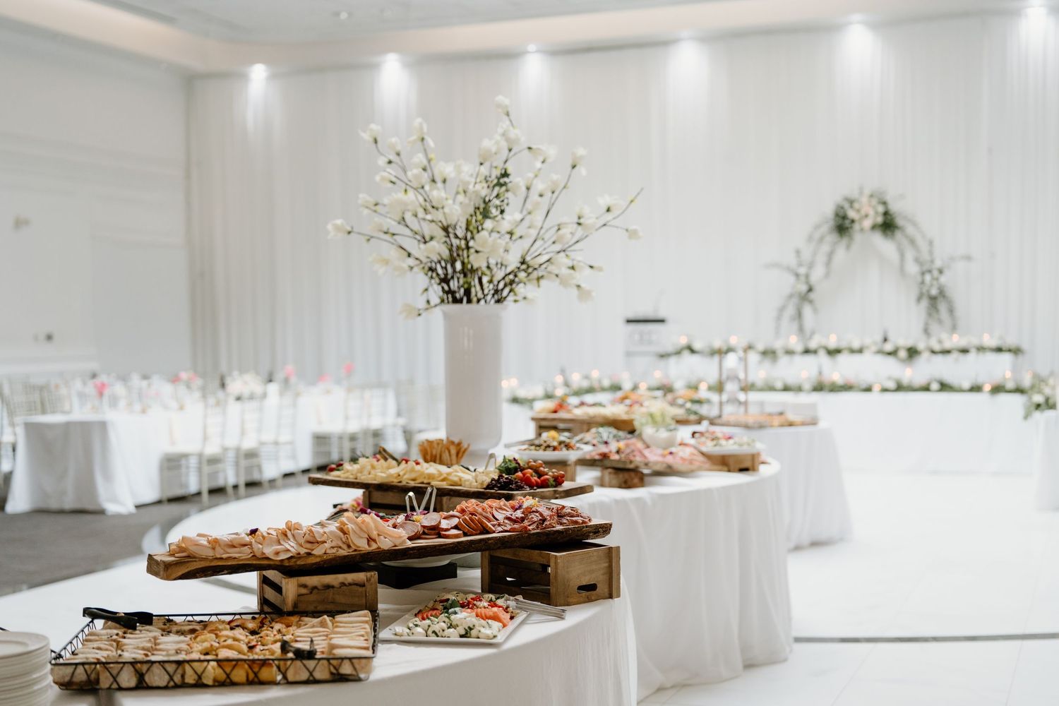 A long white table decorated with elegant floral arrangements and platters of food for a modern minimalist event.