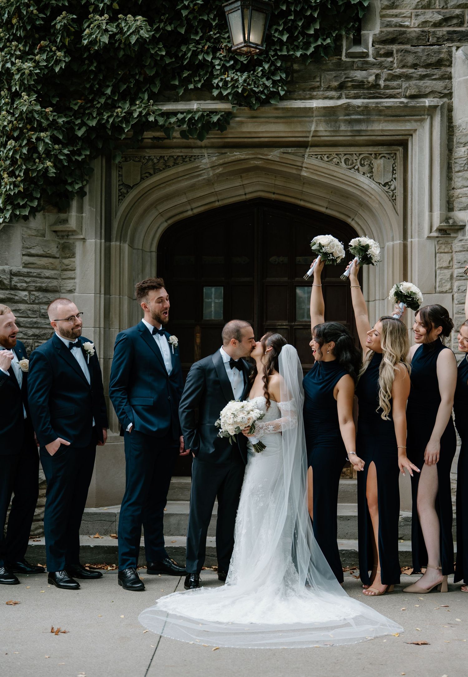 Wedding party lined up in front of stone building for creative photo sequence showing couple sharing a kiss.