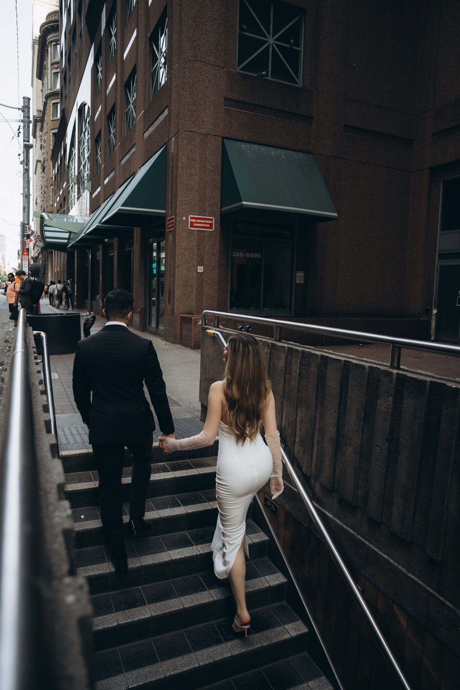 A couple walks up concrete steps between metal railings in an urban setting.