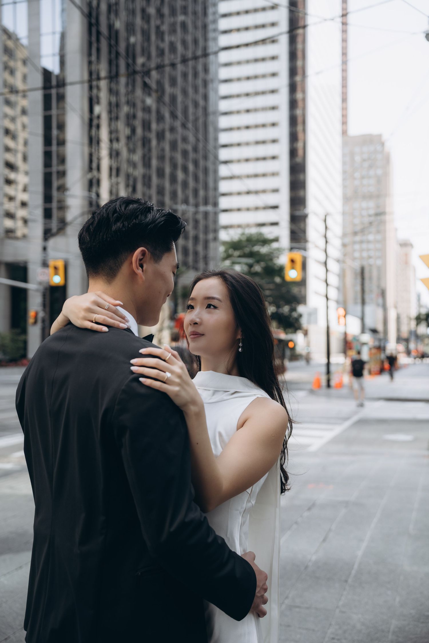 A couple embraces on a city street surrounded by modern skyscrapers and urban architecture.