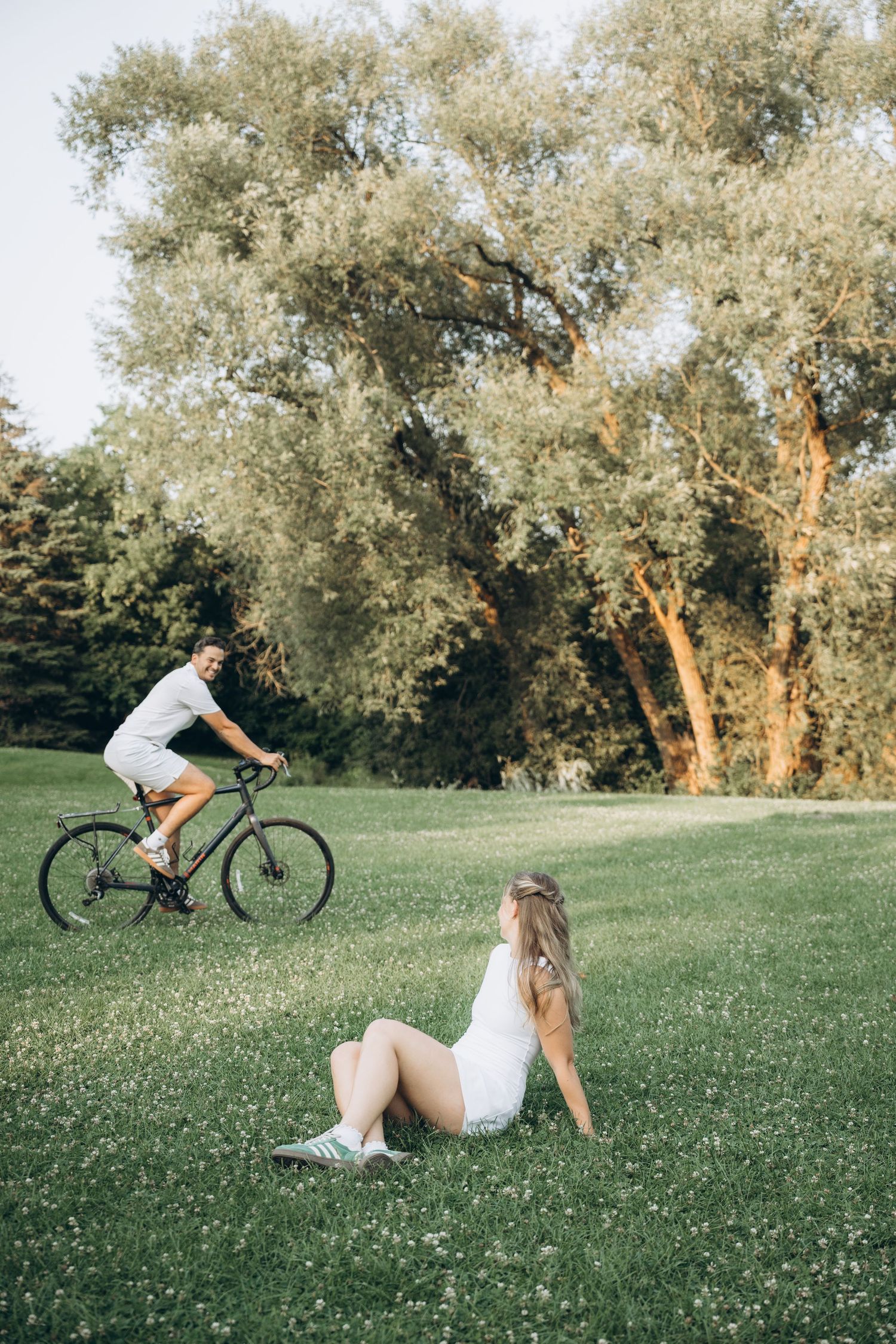 A cyclist riding and falling off their bike on a grassy hill among olive trees during golden hour.