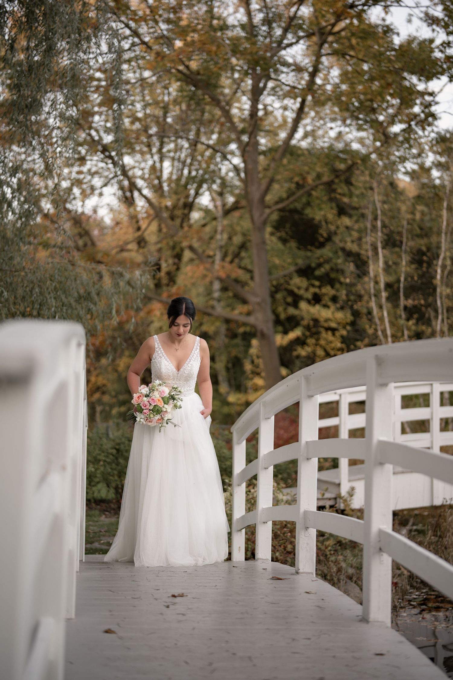 Elegant bridal portrait on a curved white bridge with fall foliage in the background.