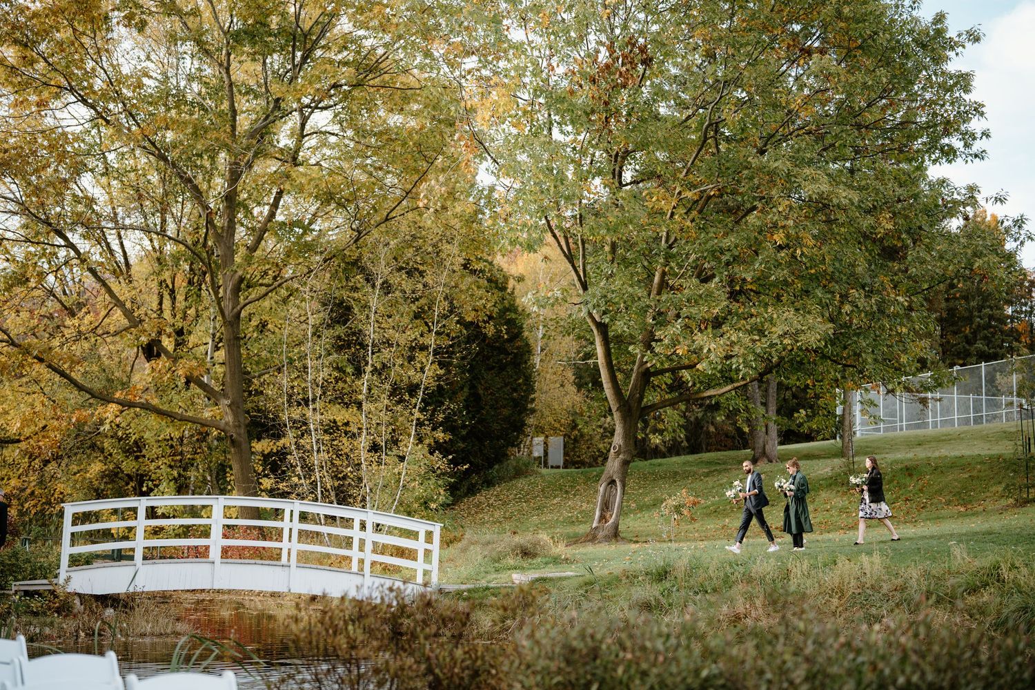 White wooden bridge crossing a pond surrounded by autumn trees and rolling hills.