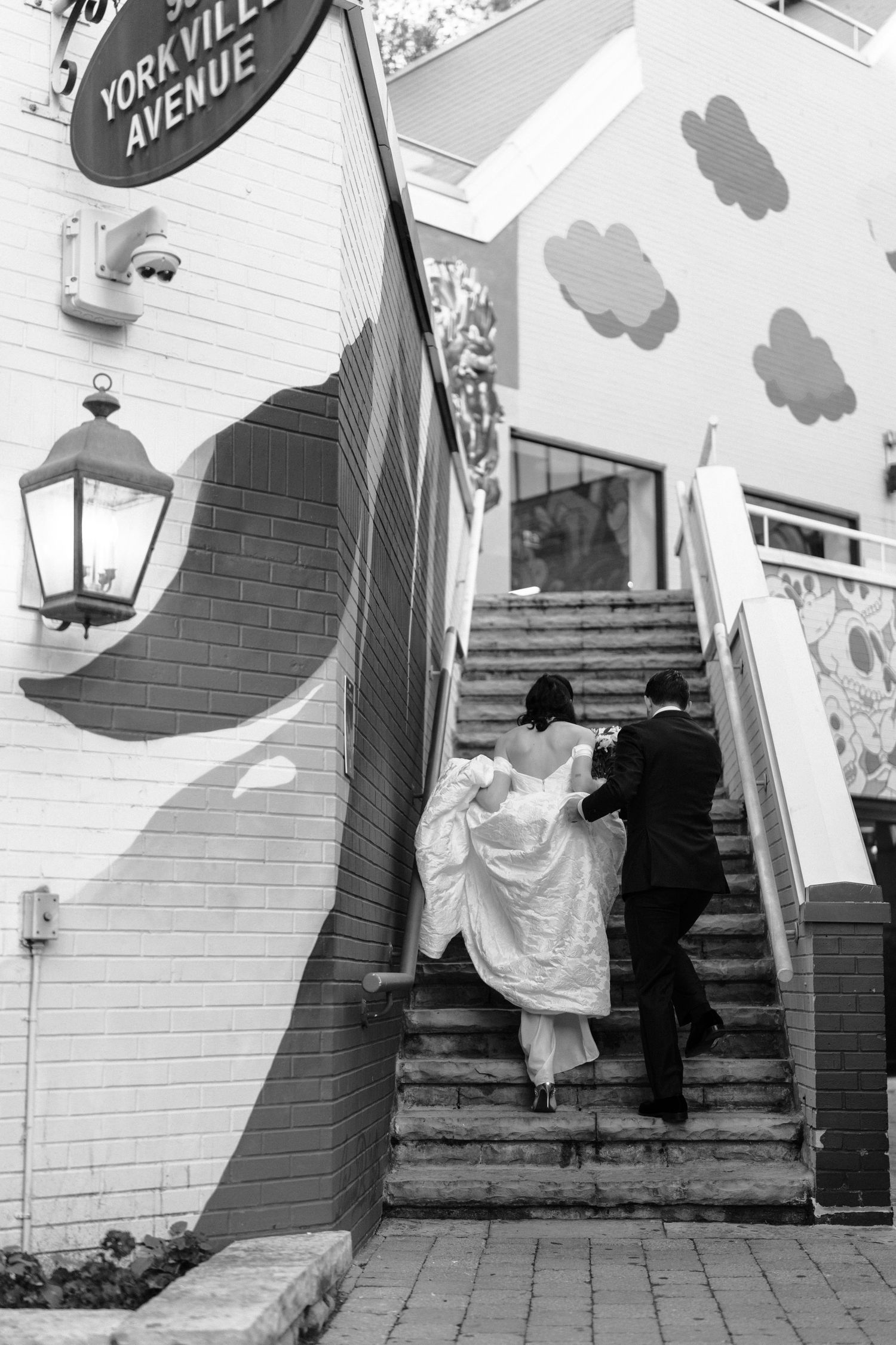 A couple in wedding attire ascends a painted staircase with artistic murals on the walls.