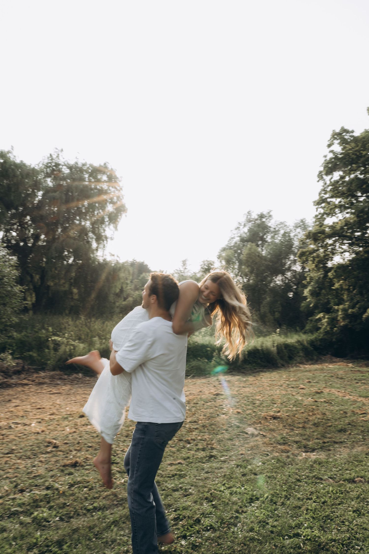 A couple dances playfully in a grassy field at sunset, creating a romantic and carefree moment.