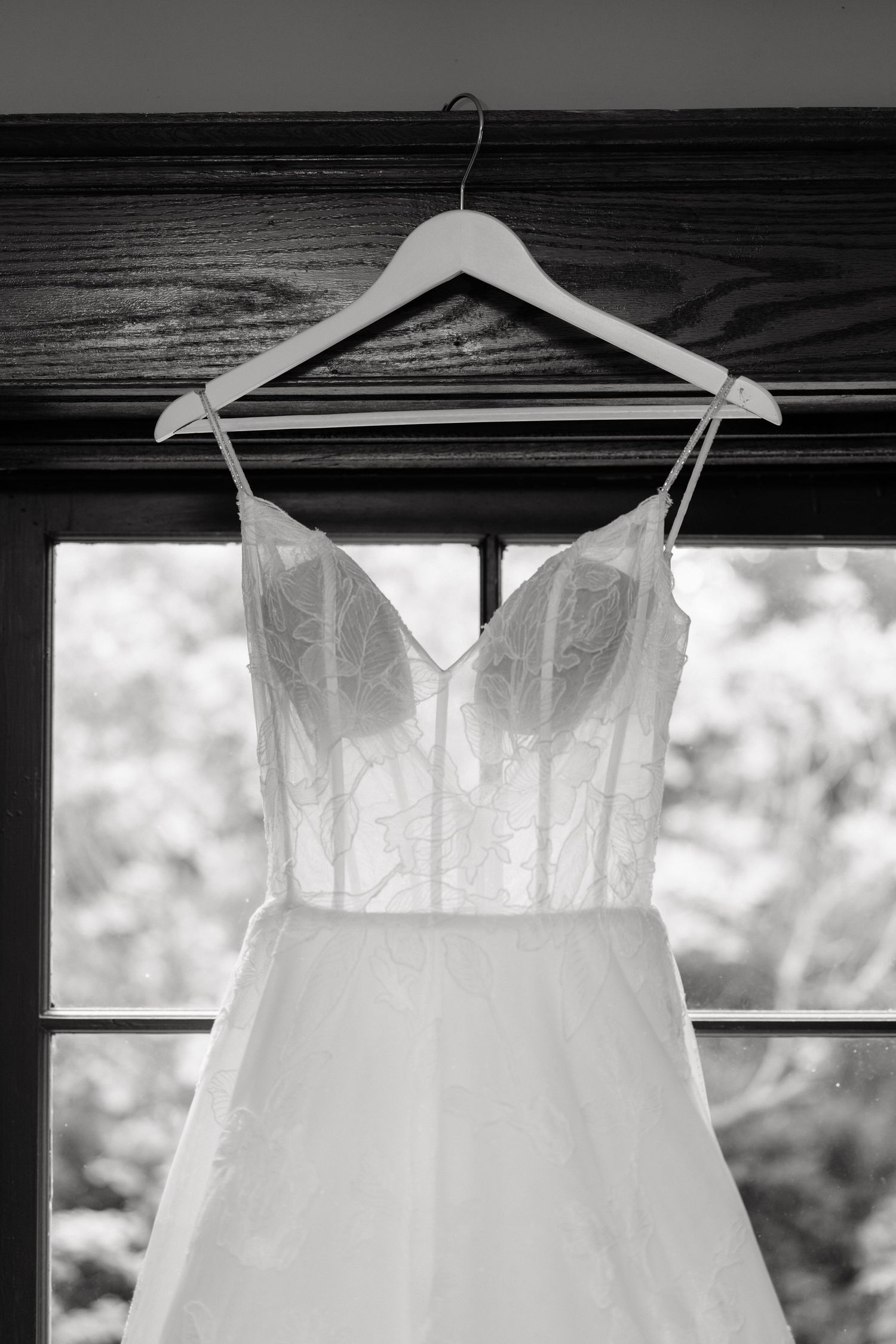 Three white wedding dresses hang on wooden hangers against a dark wall with soft natural lighting.