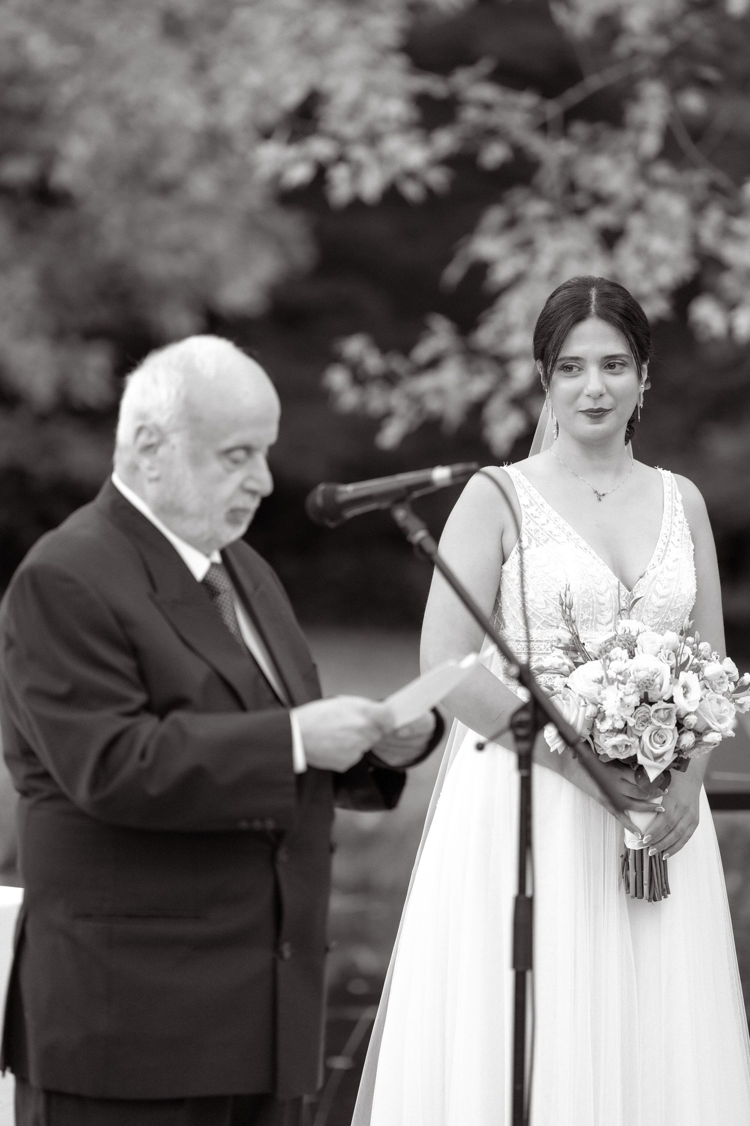 Black and white photo of wedding ceremony with officiant at microphone.