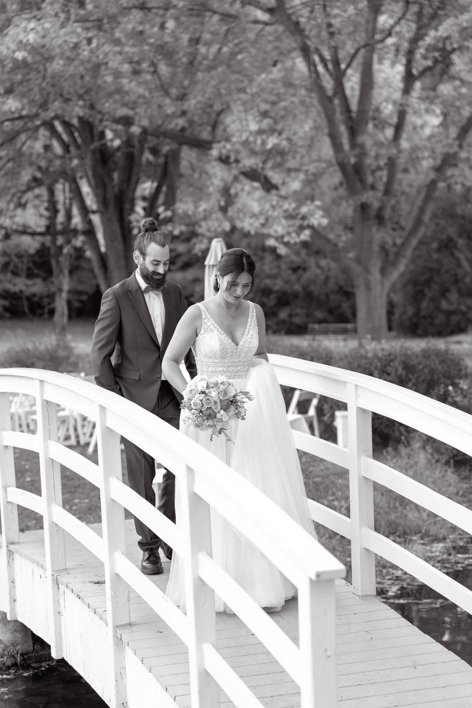 Black and white photo of wedding couple crossing an elegant white bridge in a garden setting.