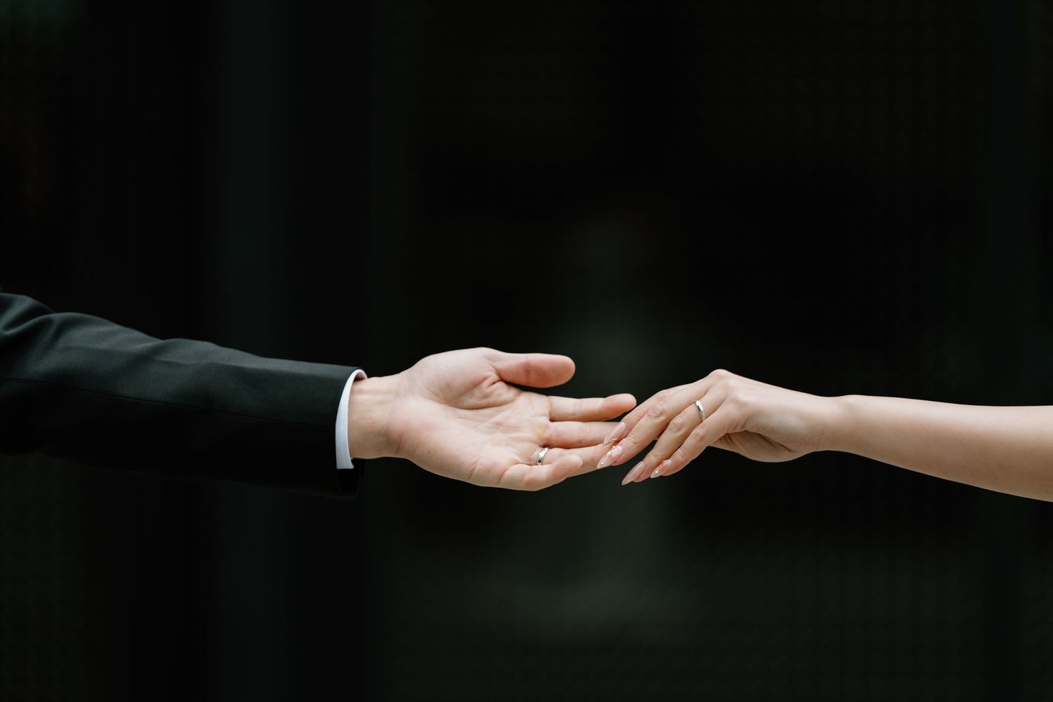 Two hands reaching towards each other against a dark background in an elegant gesture of connection.