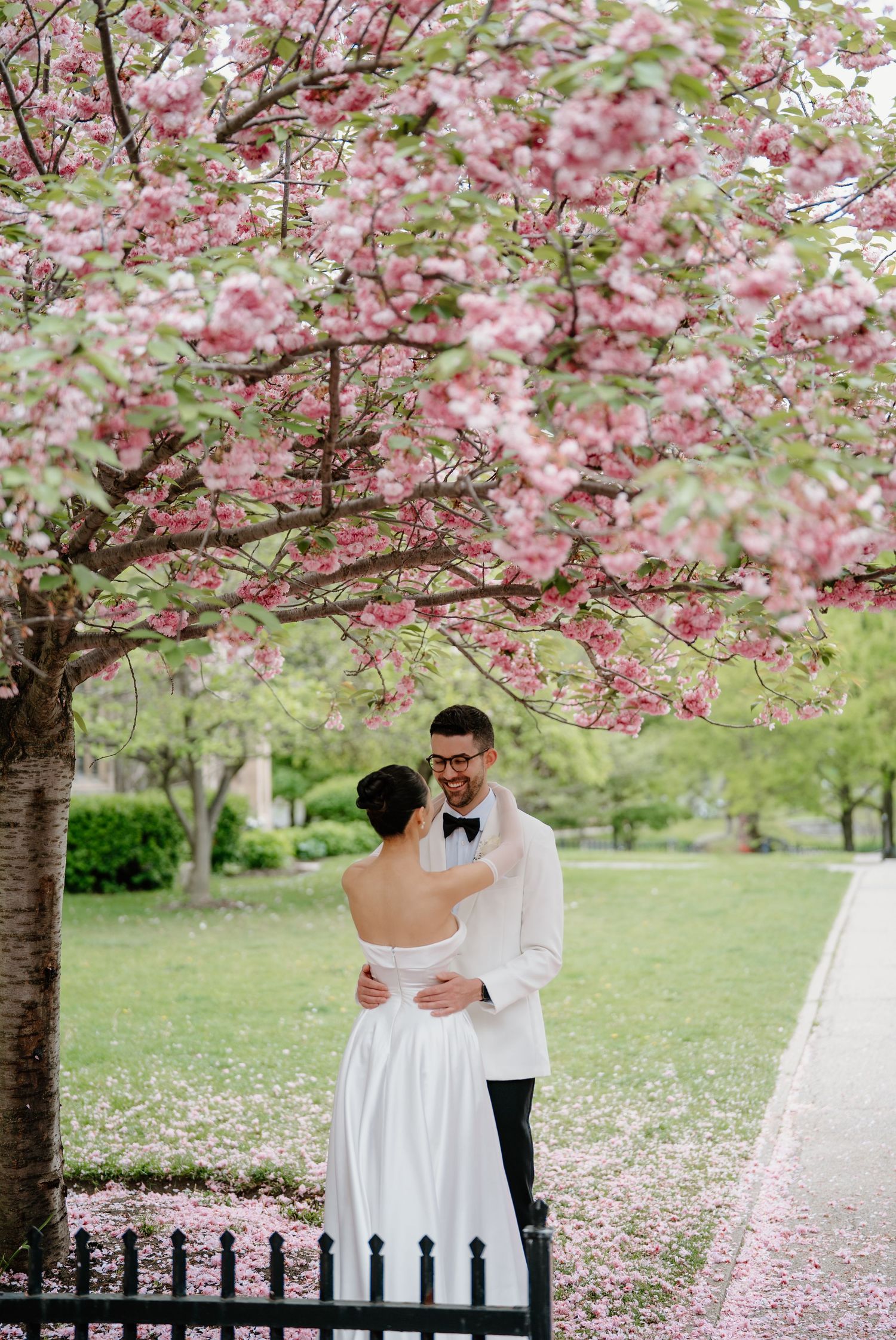 Romantic spring wedding photoshoot under pink cherry blossoms with stone building in background.