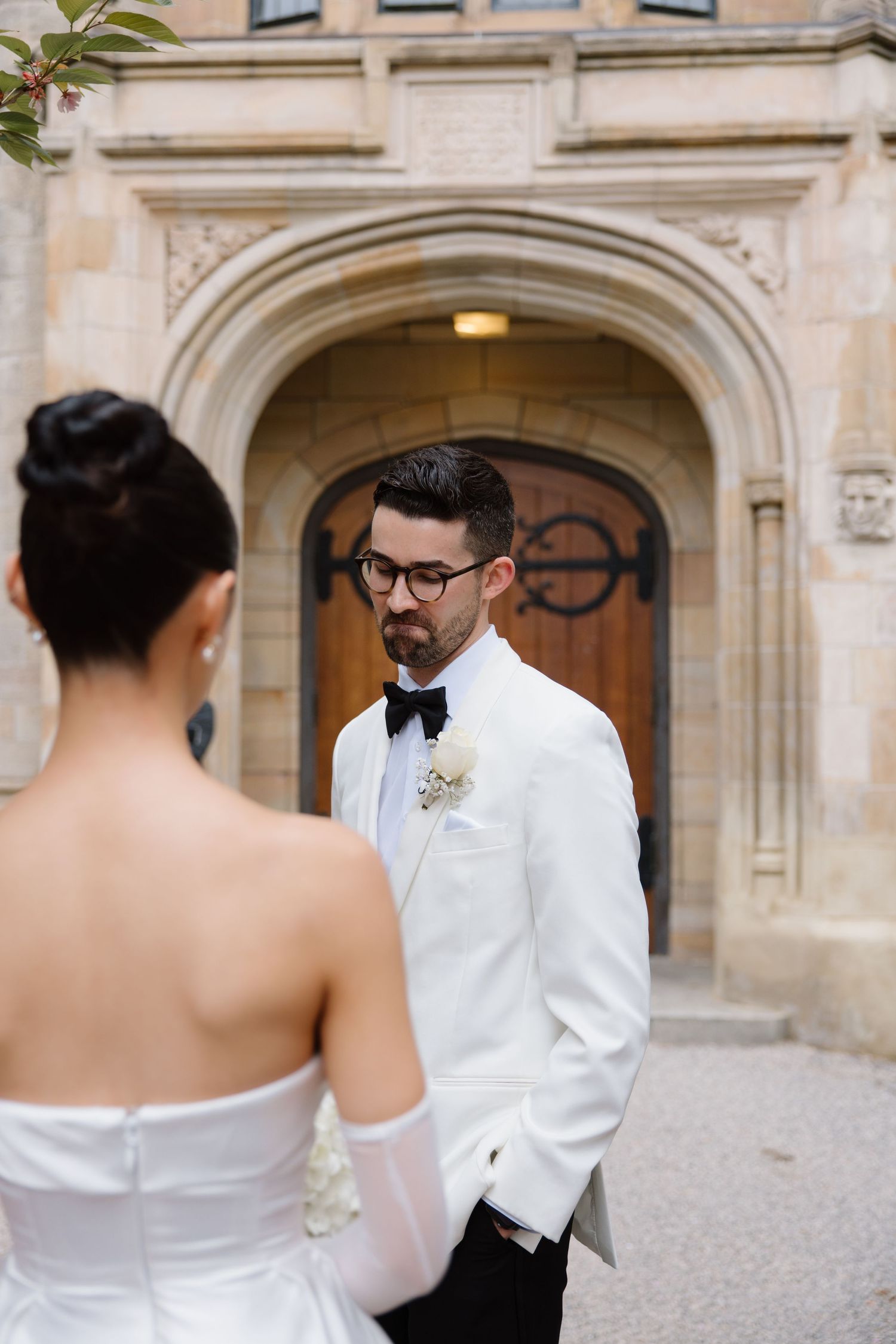 A couple shares a moment at their wedding, with the groom in white jacket by an archway entrance.