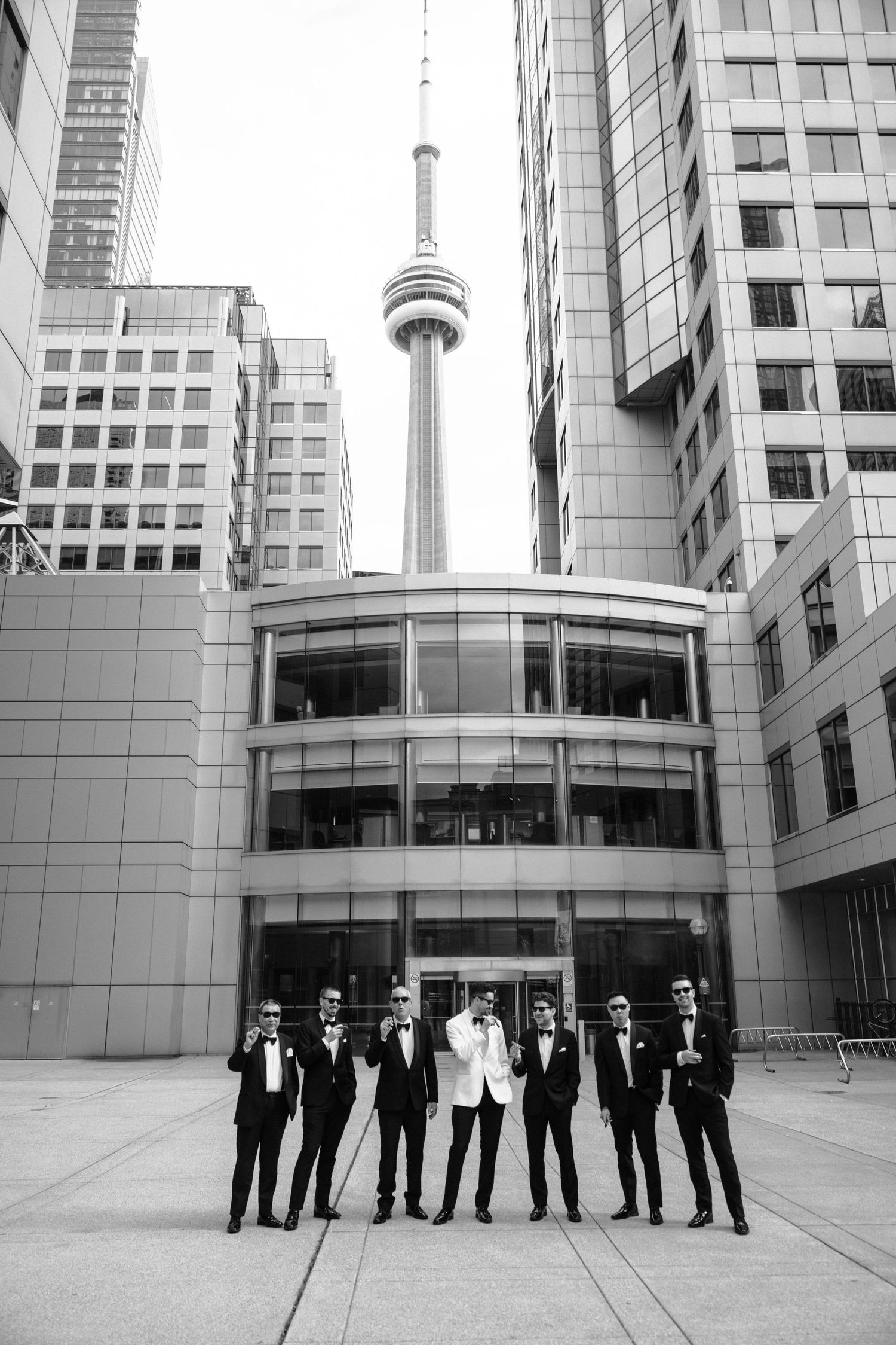 A group in formal black and white attire stands in front of modern office buildings with the CN Tower visible in downtown Toronto.