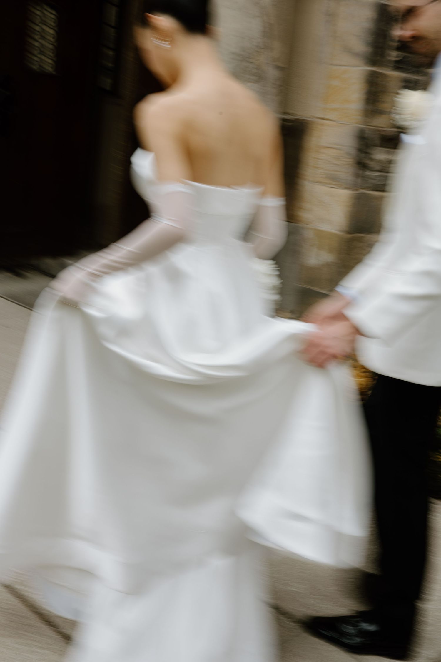 Motion-blurred artistic shot of a white wedding dress being held in an elegant stone hallway.