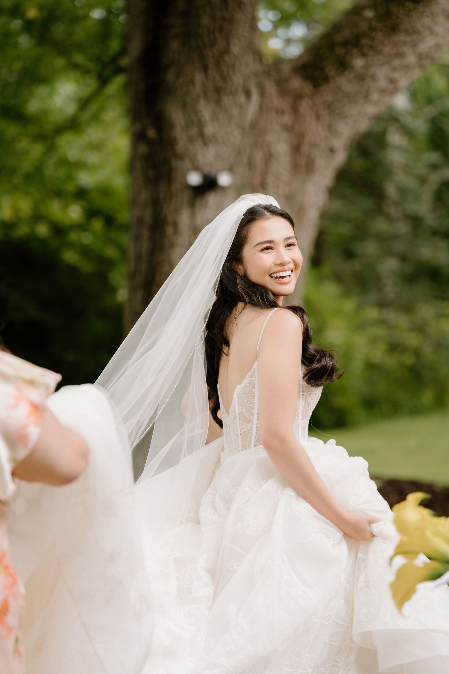 A joyful bride in a flowing white wedding dress twirls outdoors in a natural garden setting.