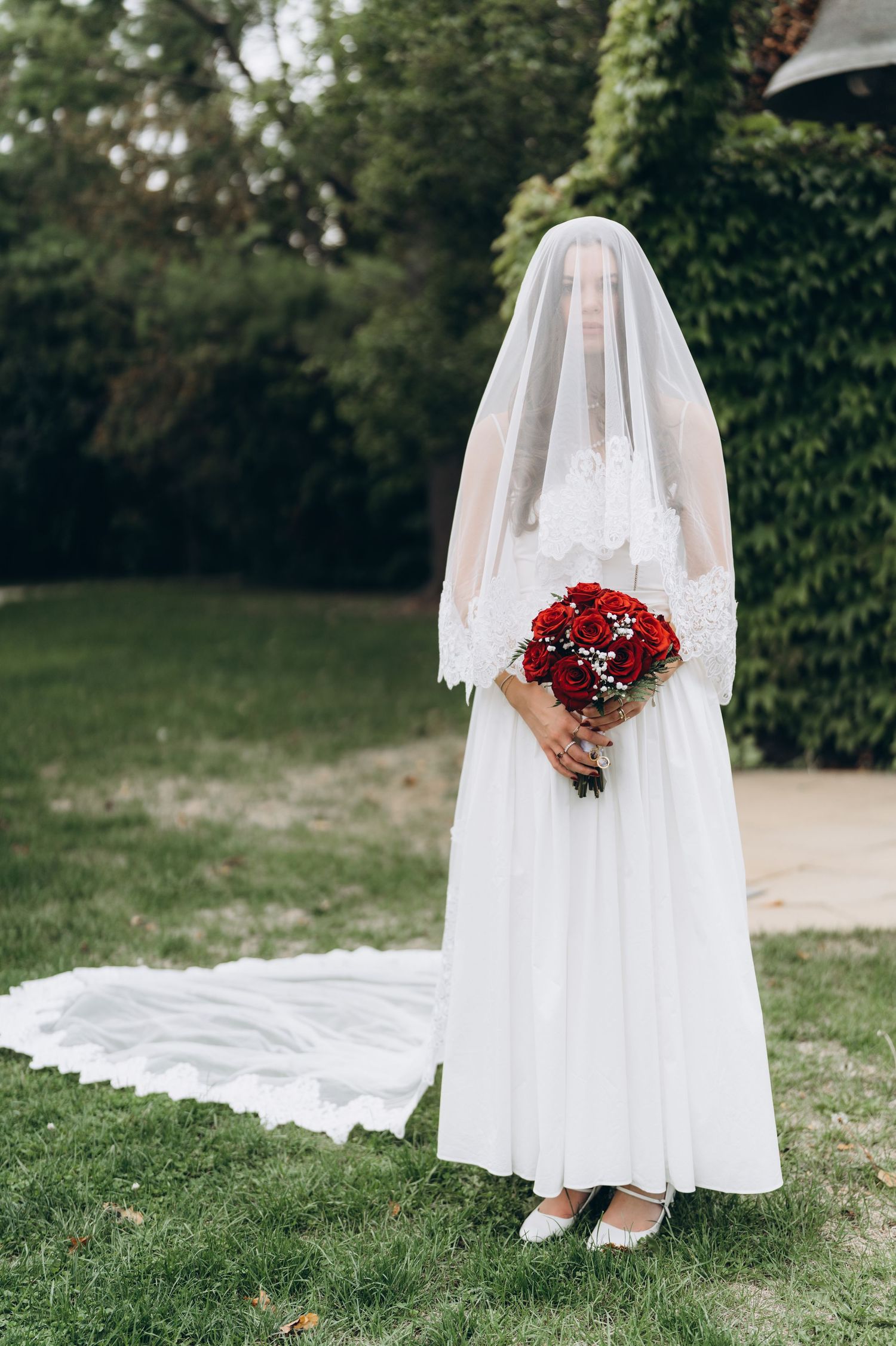 Detail shots of a white wedding dress with a cascading train and red bouquet in an outdoor garden setting.
