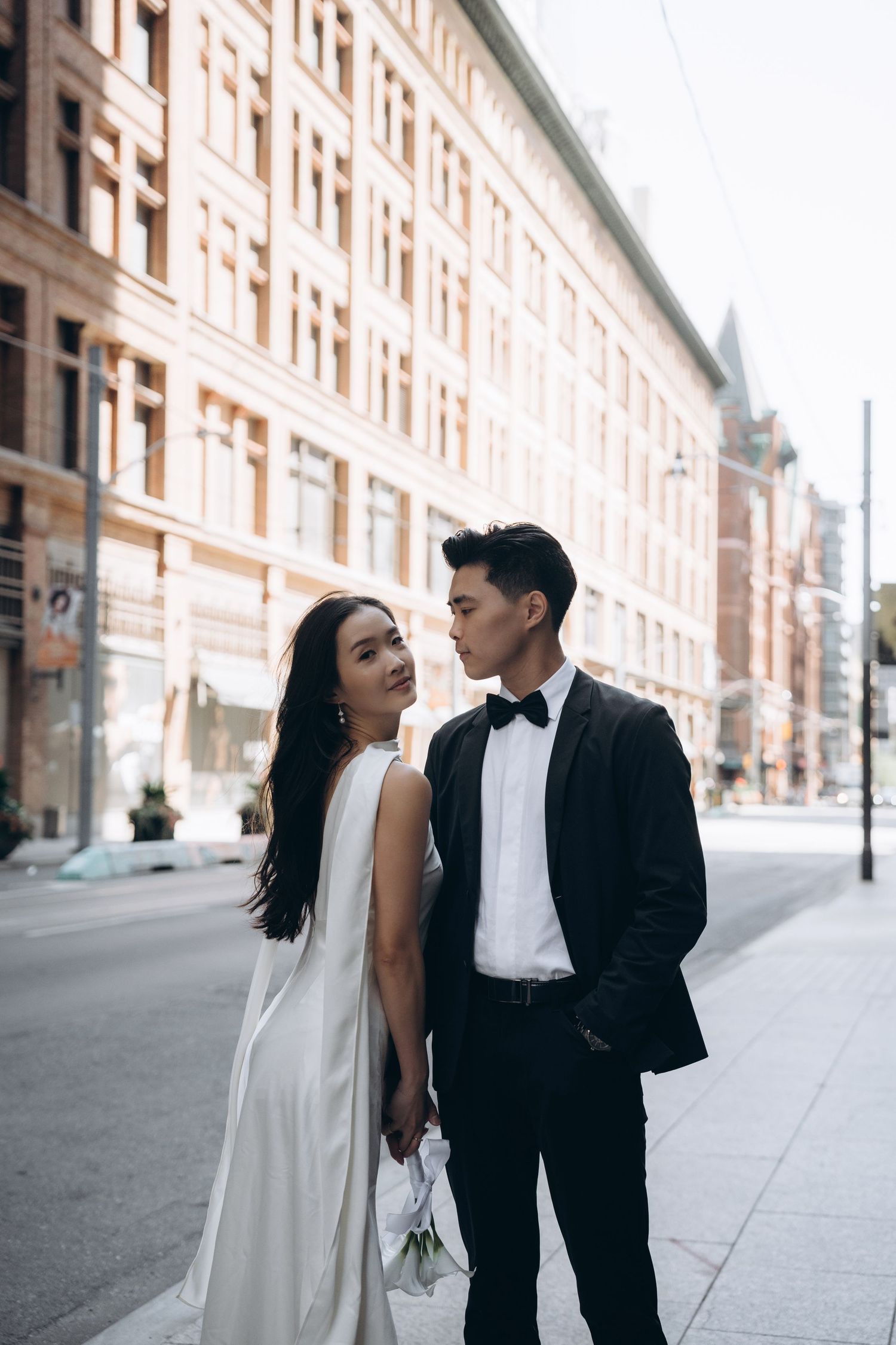 A couple in wedding attire shares tender moments in front of an elegant stone building facade.