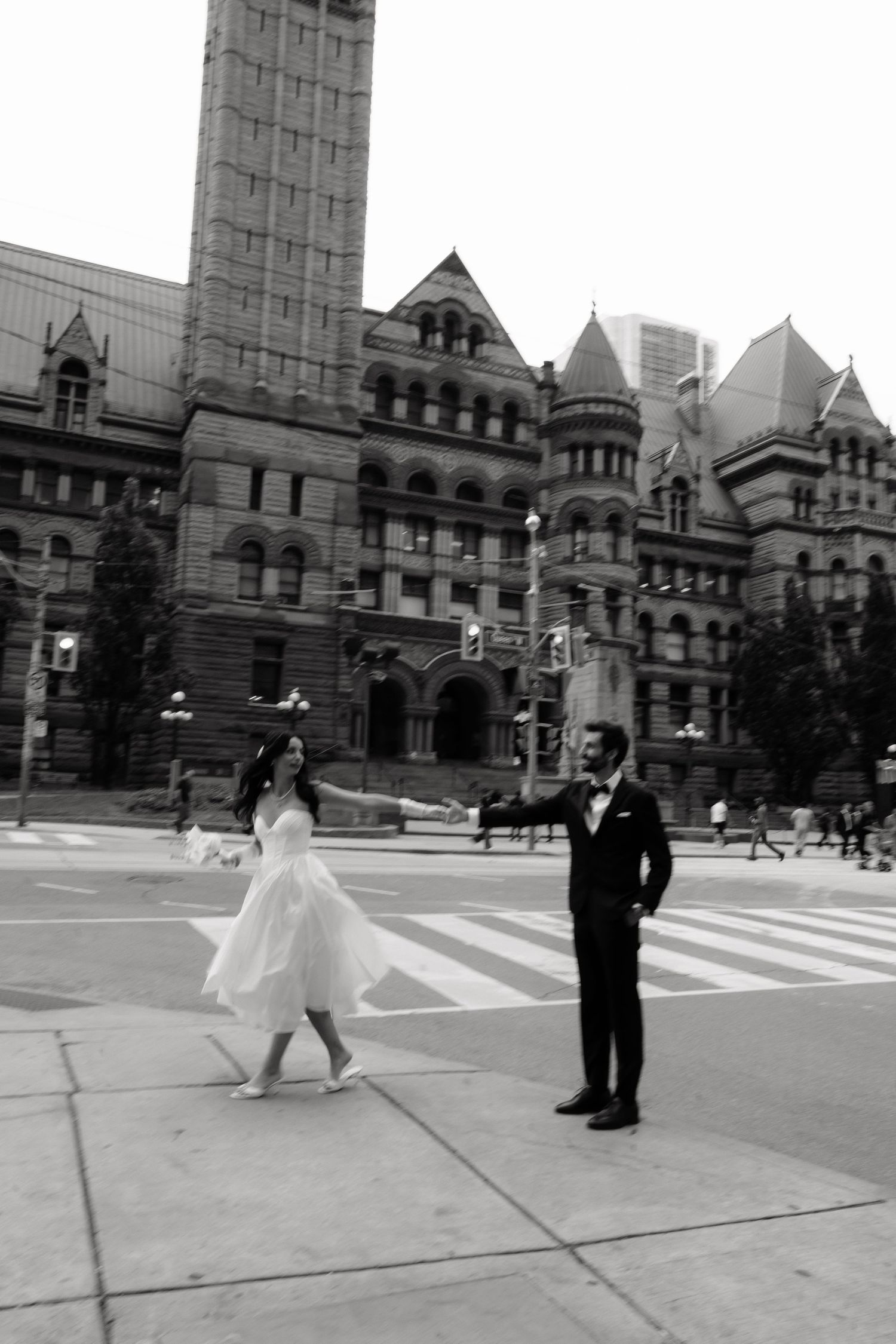 A couple in wedding attire poses in front of Toronto's Old City Hall, a historic Romanesque Revival building.