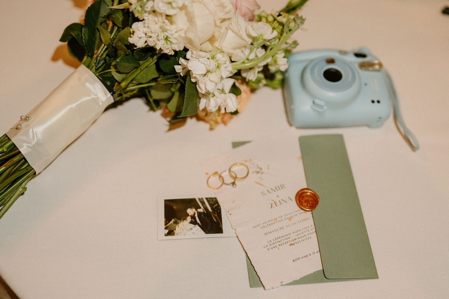 Wedding details featuring a light blue Instax camera, invitation, and white floral bouquet.