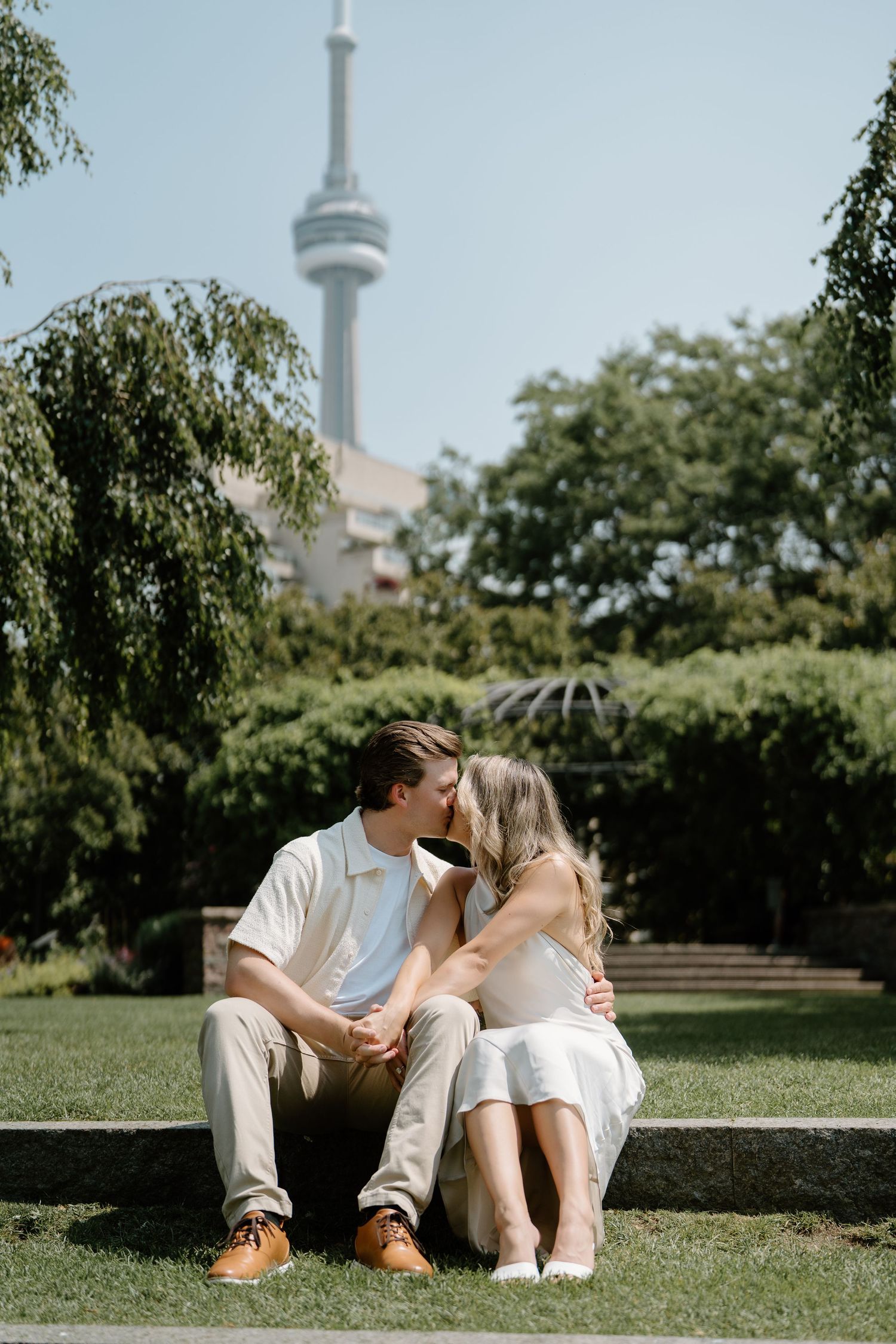 A tender moment shared on the grass with Toronto's iconic CN Tower rising in the distance.