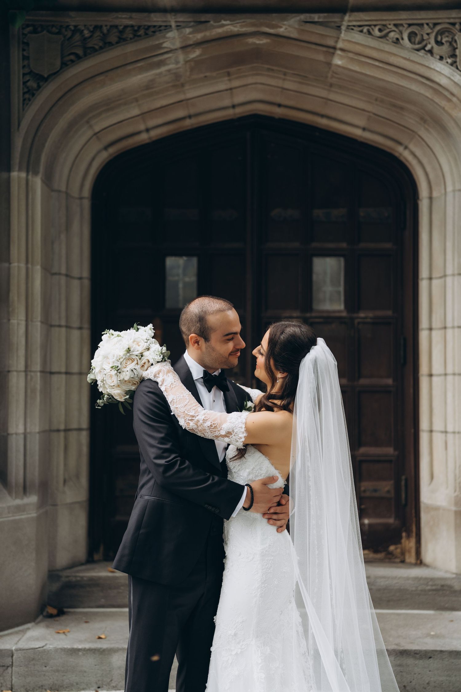 A romantic wedding moment captured in front of an ornate stone church doorway.