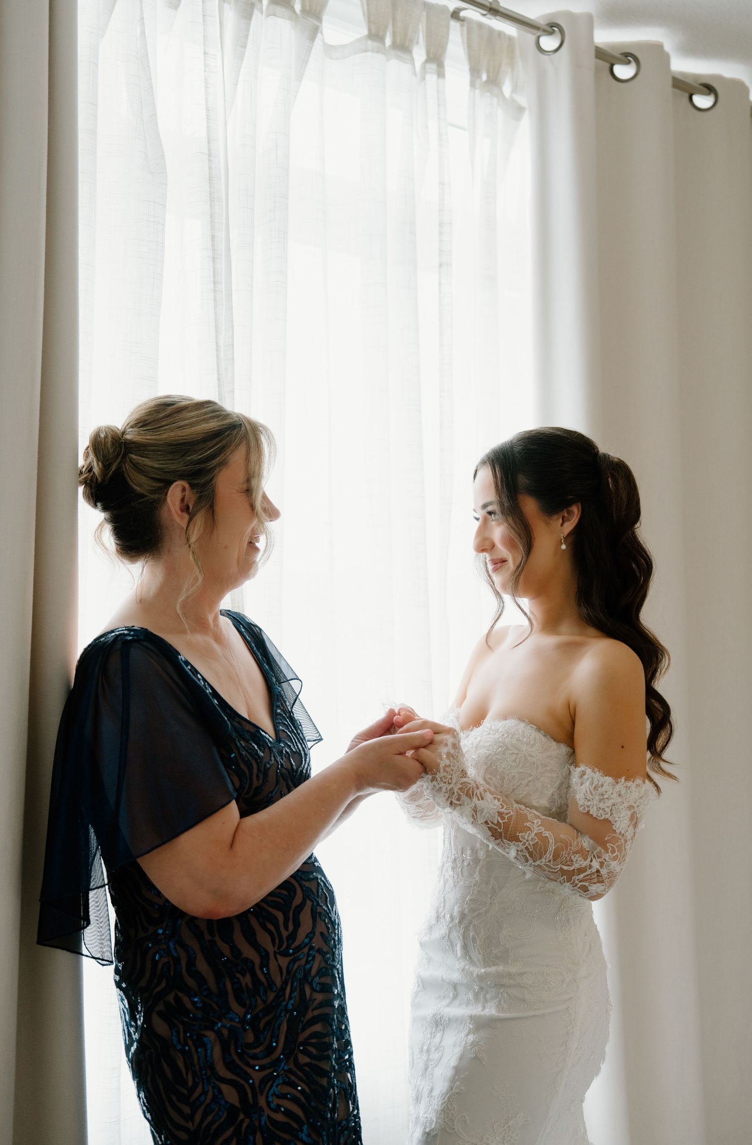 A series of candid moments showing a bride getting dressed with help from someone in a dark dress by a window.