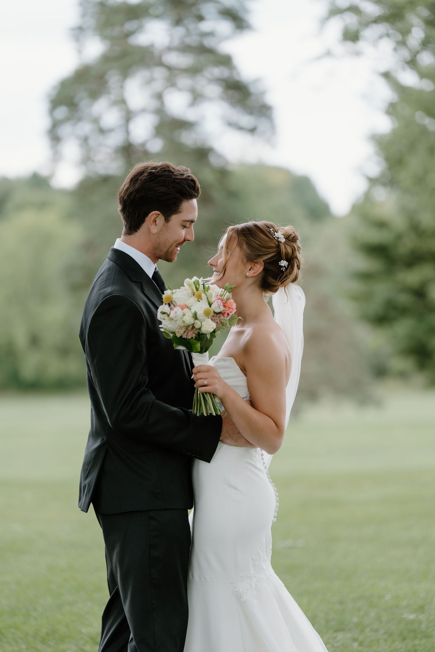 A bride and groom share an intimate moment together on a grassy lawn with a bouquet of pastel flowers.