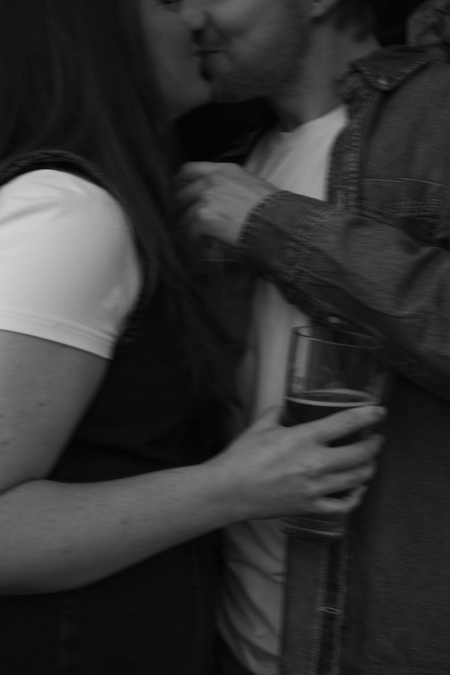 A grayscale close-up of two people holding a glass in a dimly lit setting.