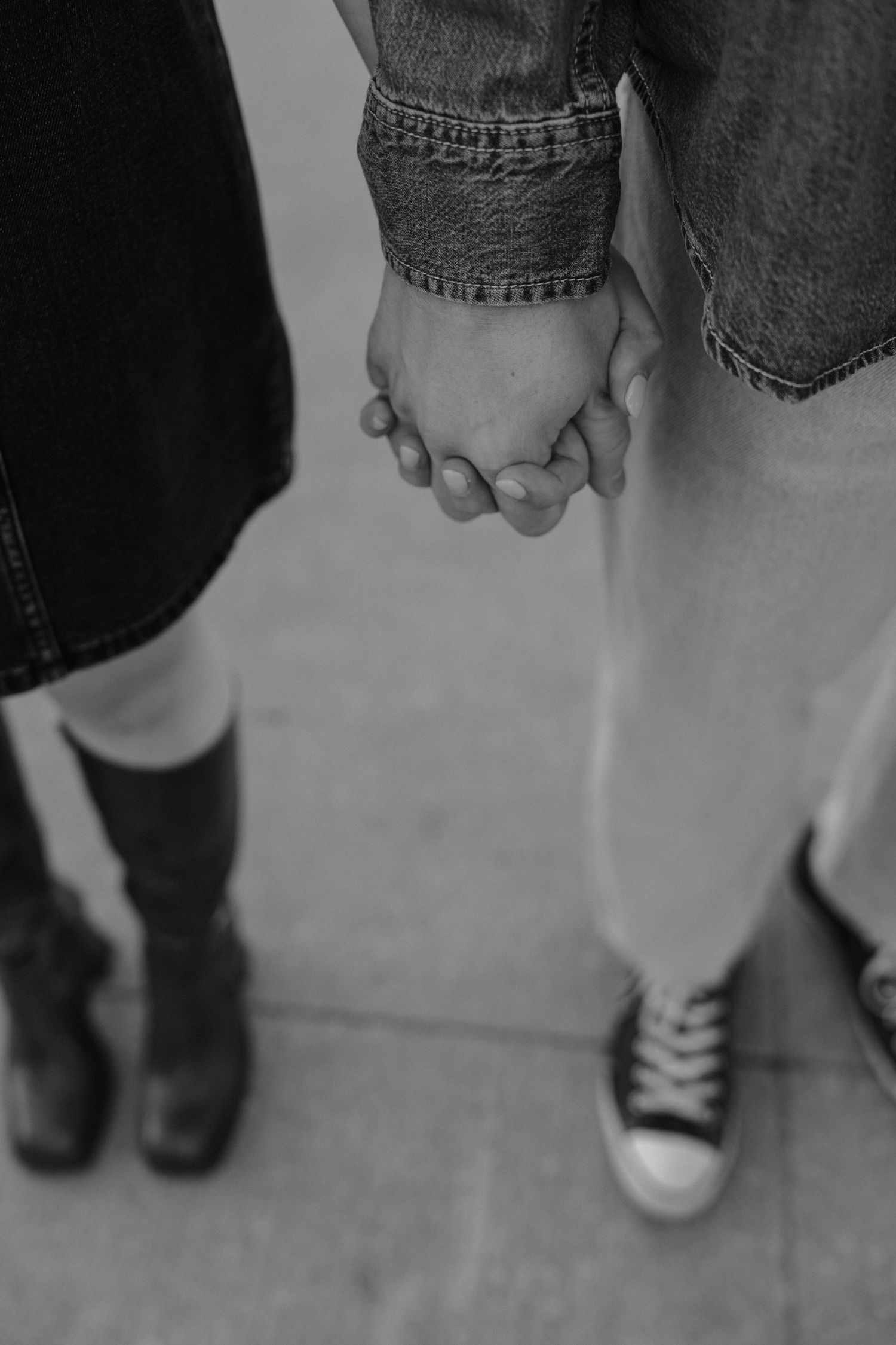 Black and white image of two people holding hands while wearing jeans and casual shoes.