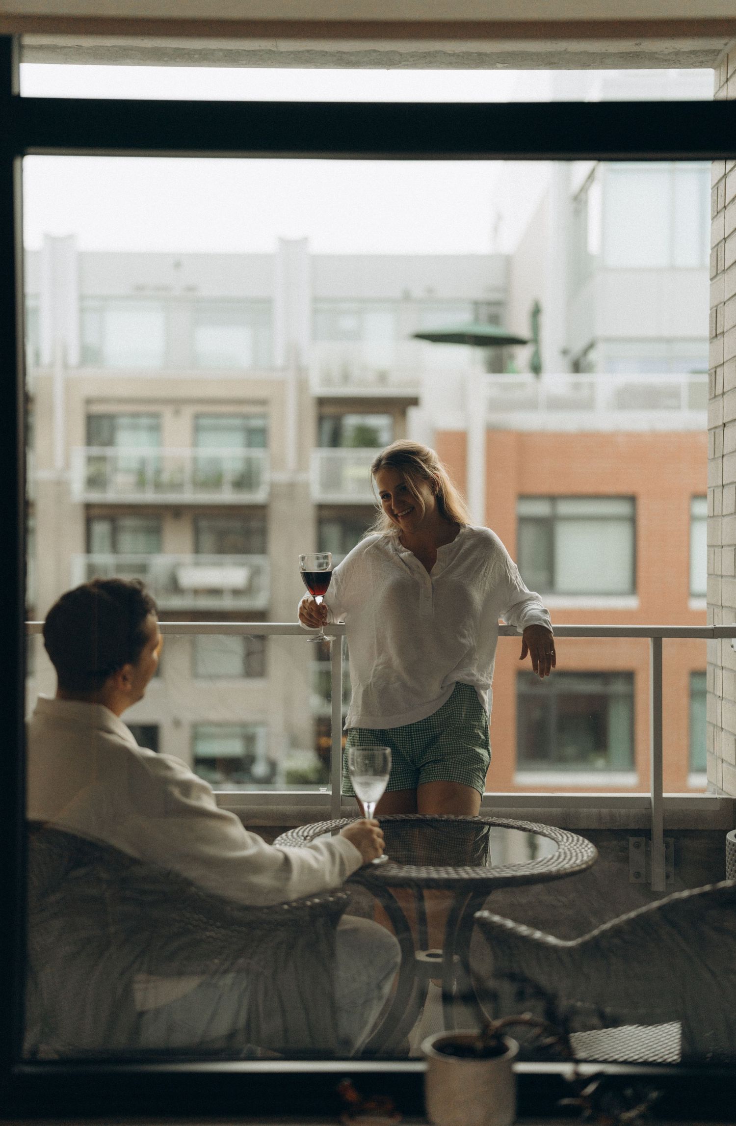 Two people enjoying wine on an urban balcony with city buildings visible in the background.