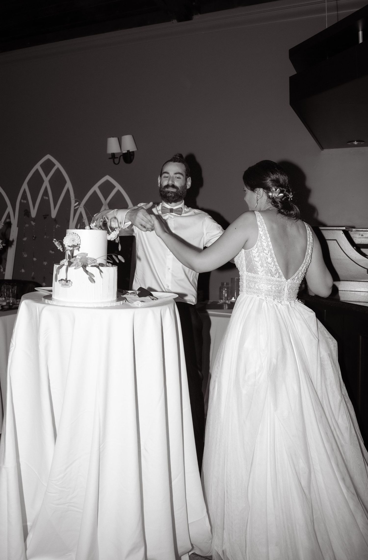 A black and white photo of newlyweds sharing a playful moment while cutting their wedding cake.