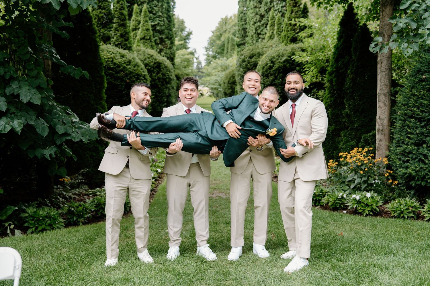Groomsmen in khaki pants perform playful poses in a lush garden setting during a wedding photo session.