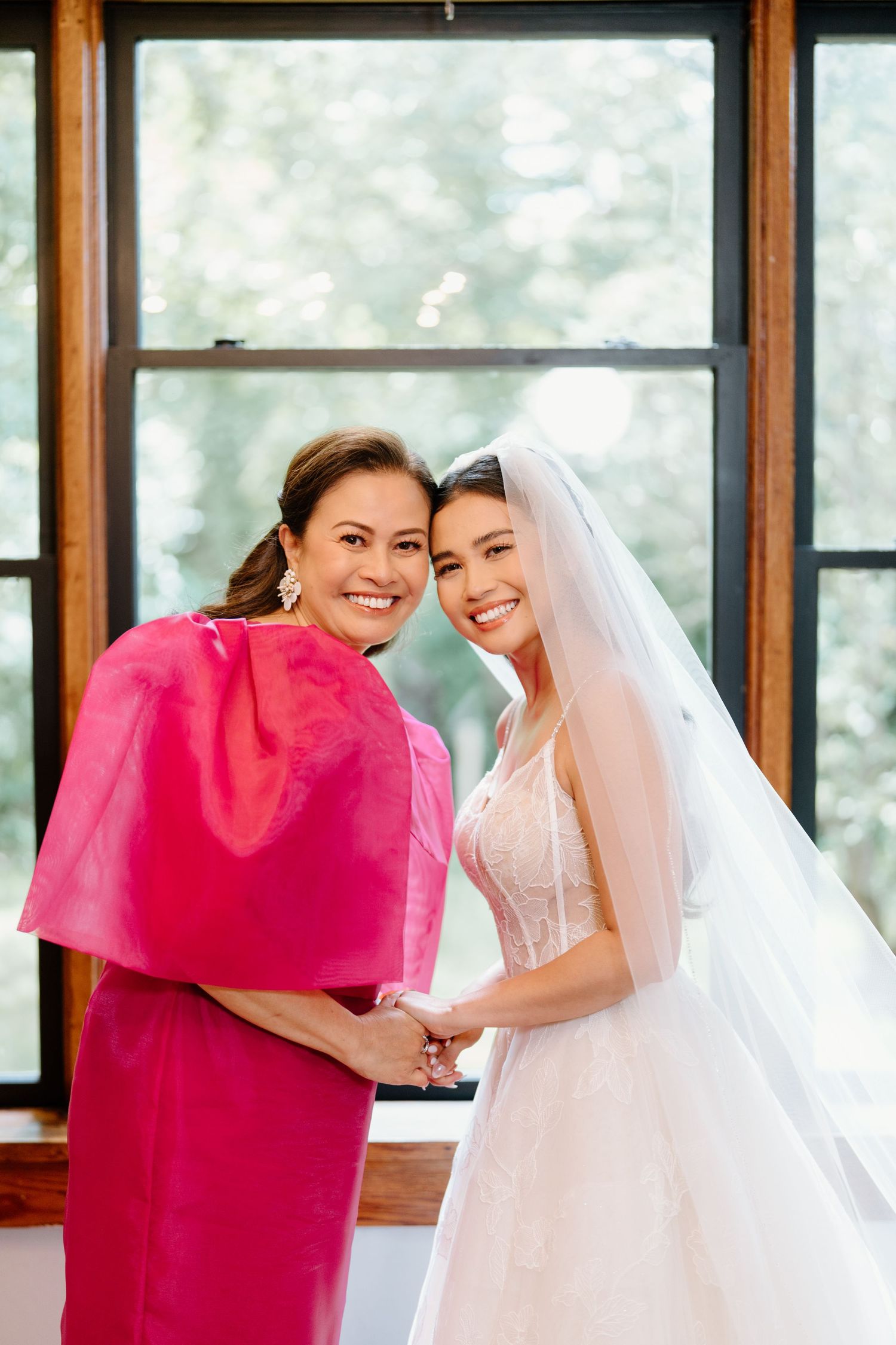 A bride in white dress and veil shares joyful moments with attendants in bright pink dresses at a wedding celebration.