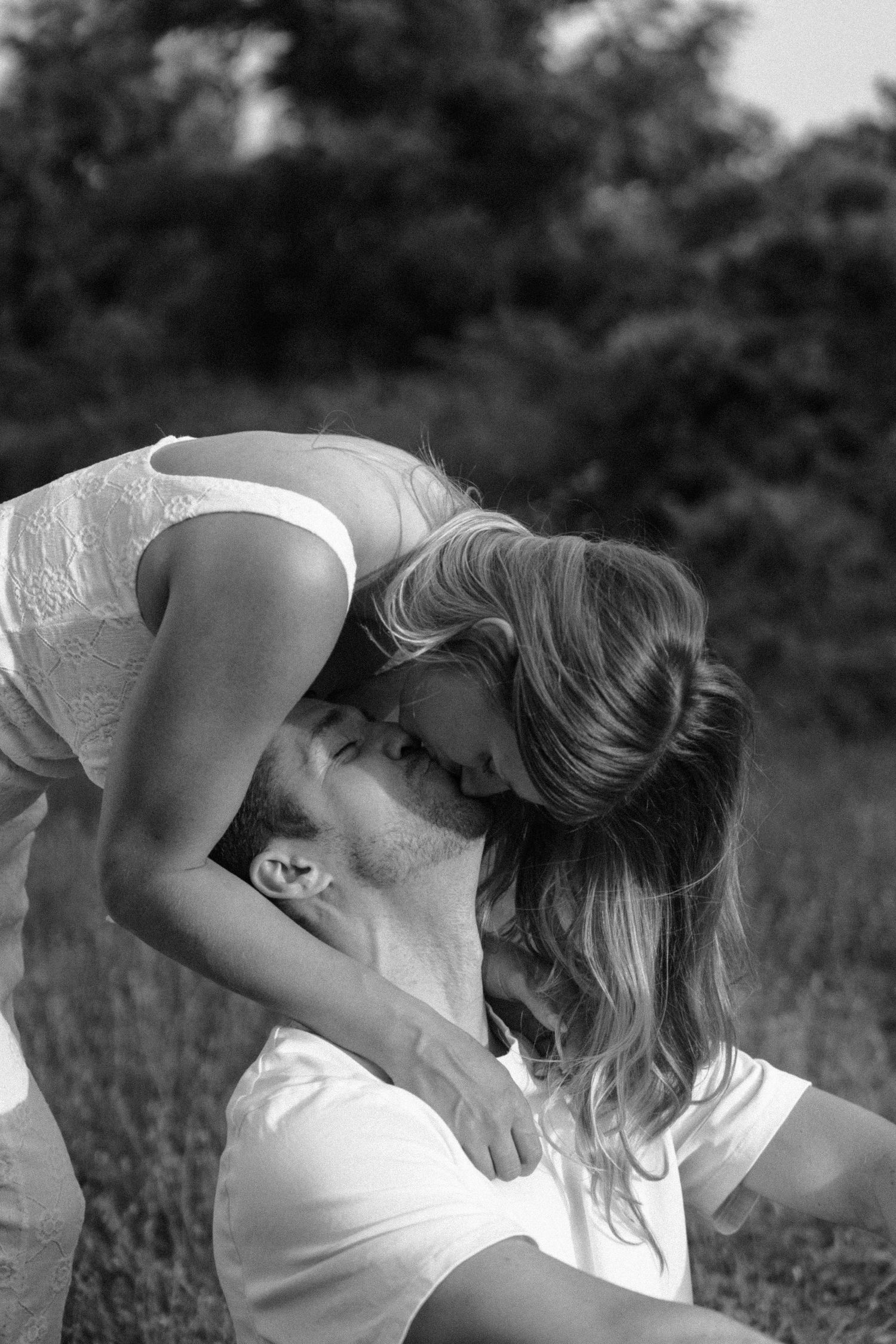 Black and white photo sequence showing a couple leaning in for a passionate kiss in a field.