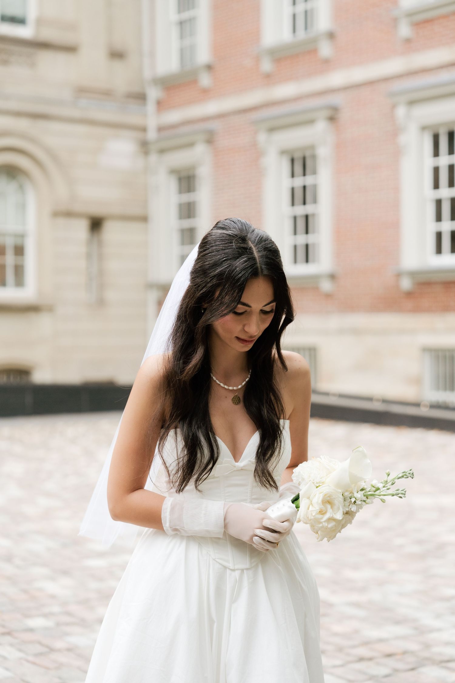 A woman in a flowing white dress poses gracefully against a pink stone building exterior.