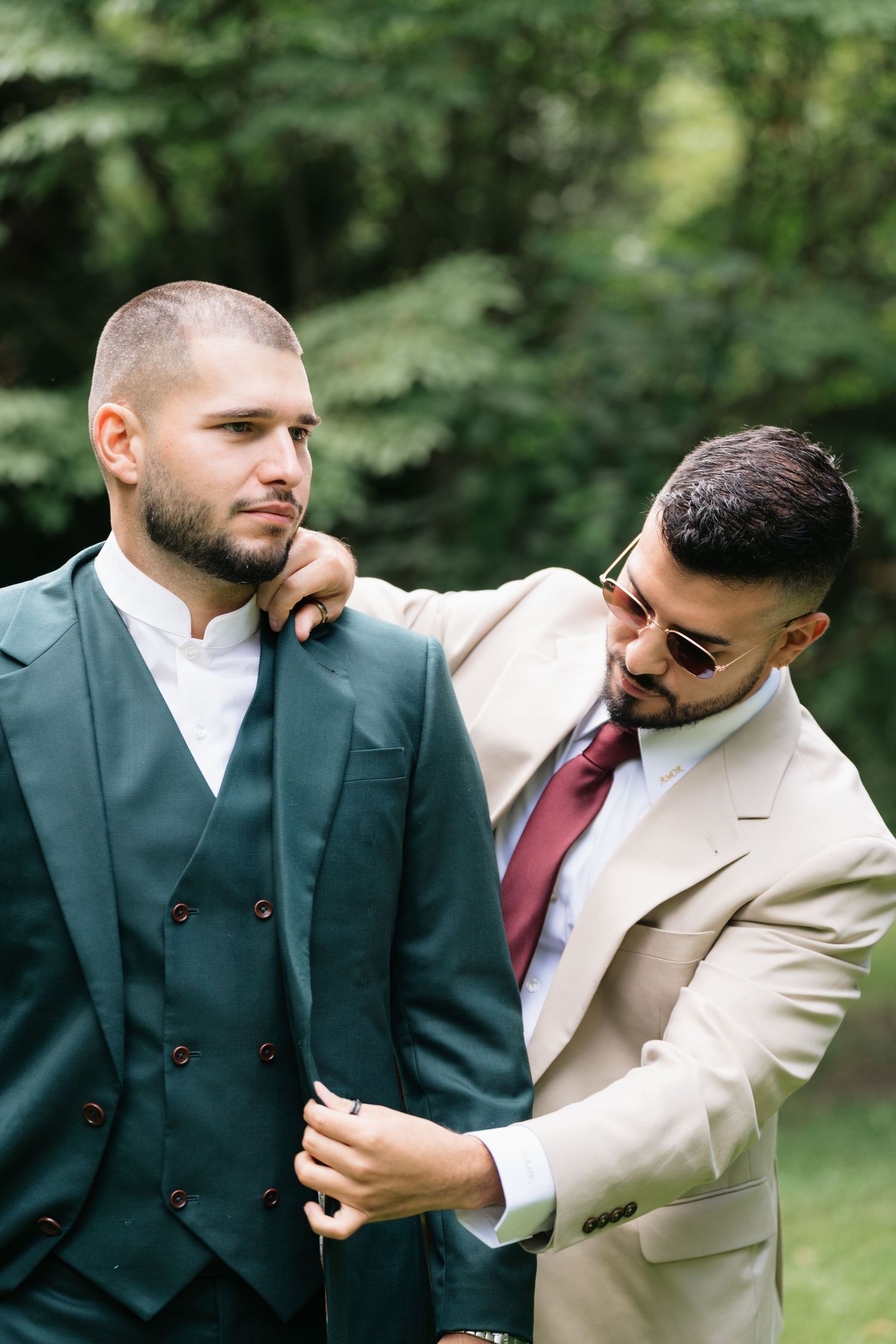Two groomsmen in contrasting dark and light suits share a playful moment during wedding photos in an outdoor setting.