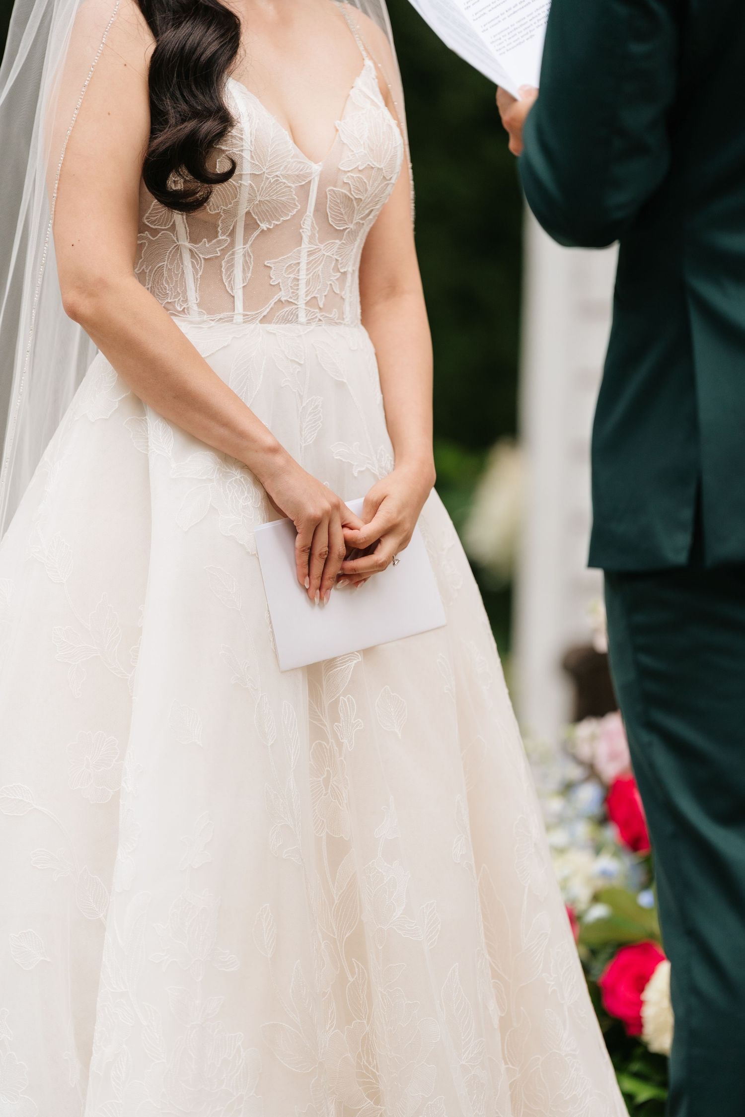Close-up of a bride in a delicate lace corset wedding dress holding a white envelope during the ceremony.