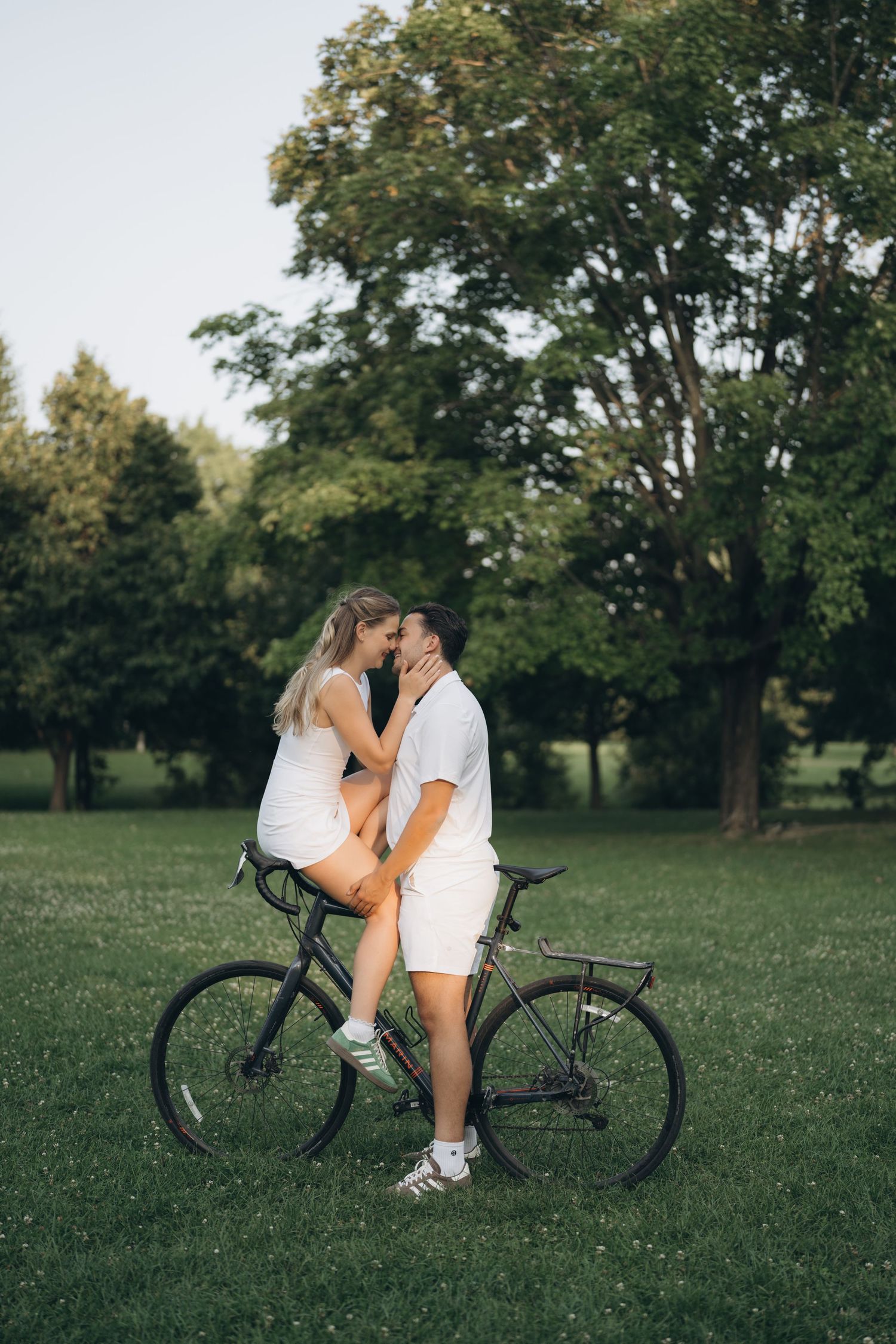 Romantic couple on a warm summer day sharing an intimate moment with a bicycle in a lush green park setting.
