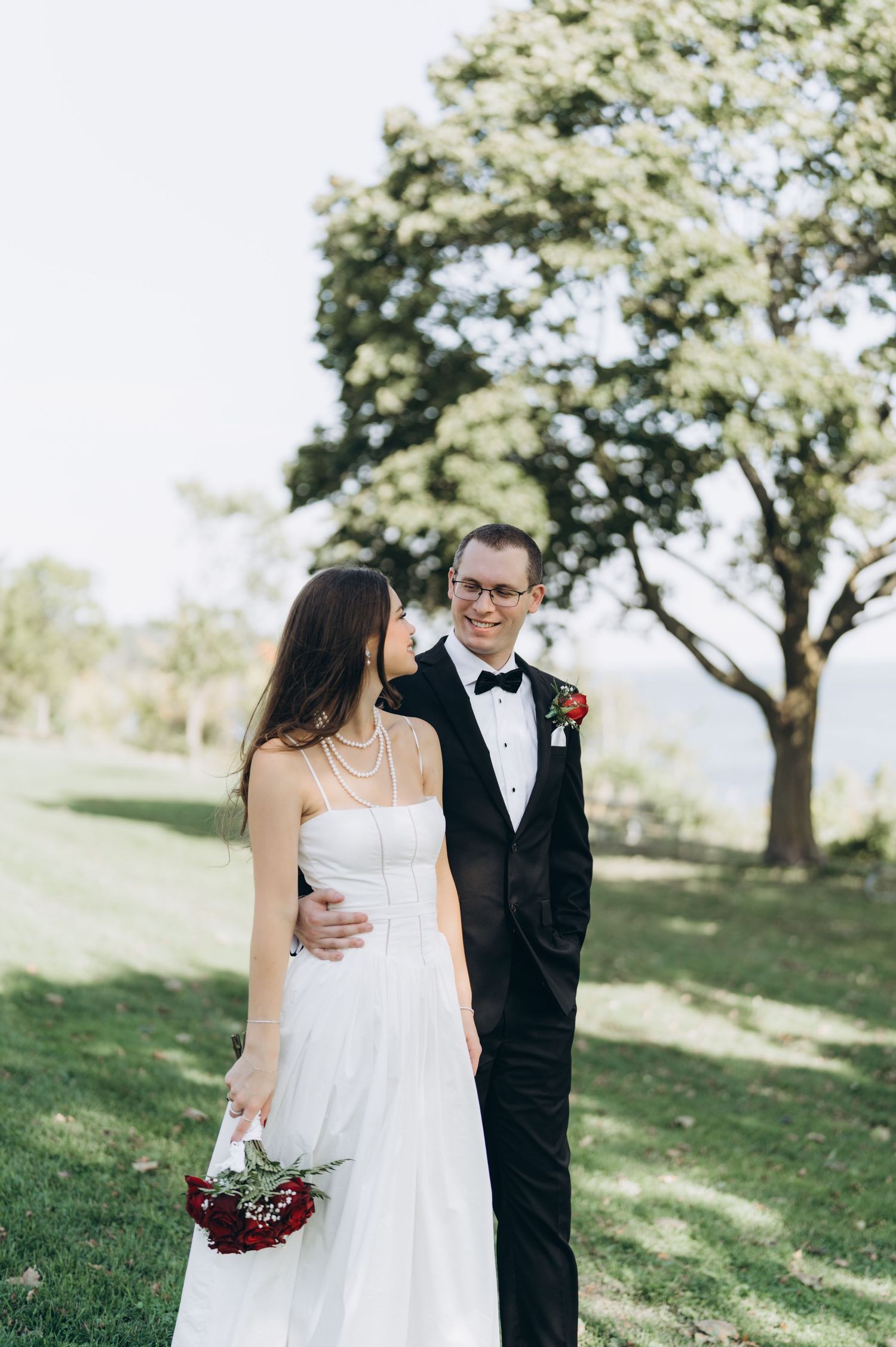 Newlyweds share intimate moments in an outdoor garden setting with blooming trees and natural sunlight.