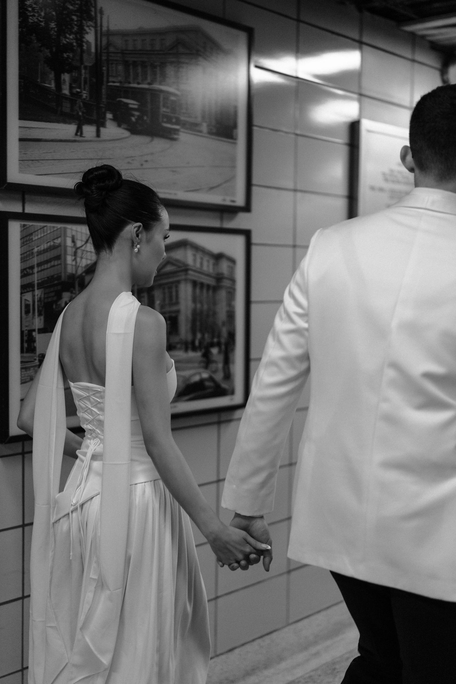 Black and white photograph showing people walking in a subway station corridor with artwork displayed on the walls.