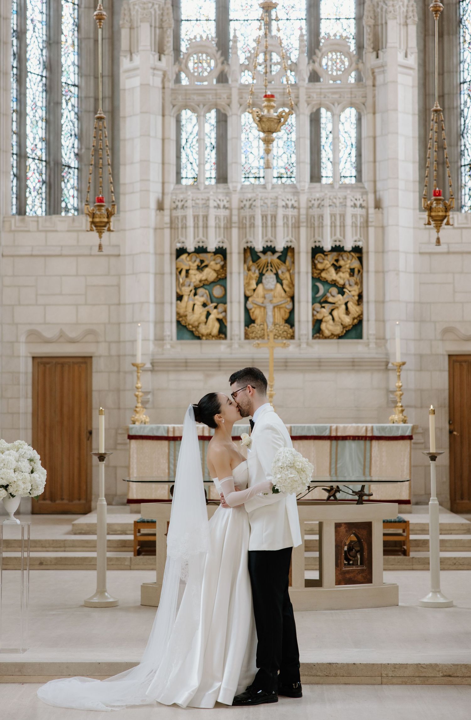 A couple shares an intimate moment during their wedding ceremony in an elegant church with gothic architecture and stained glass windows.