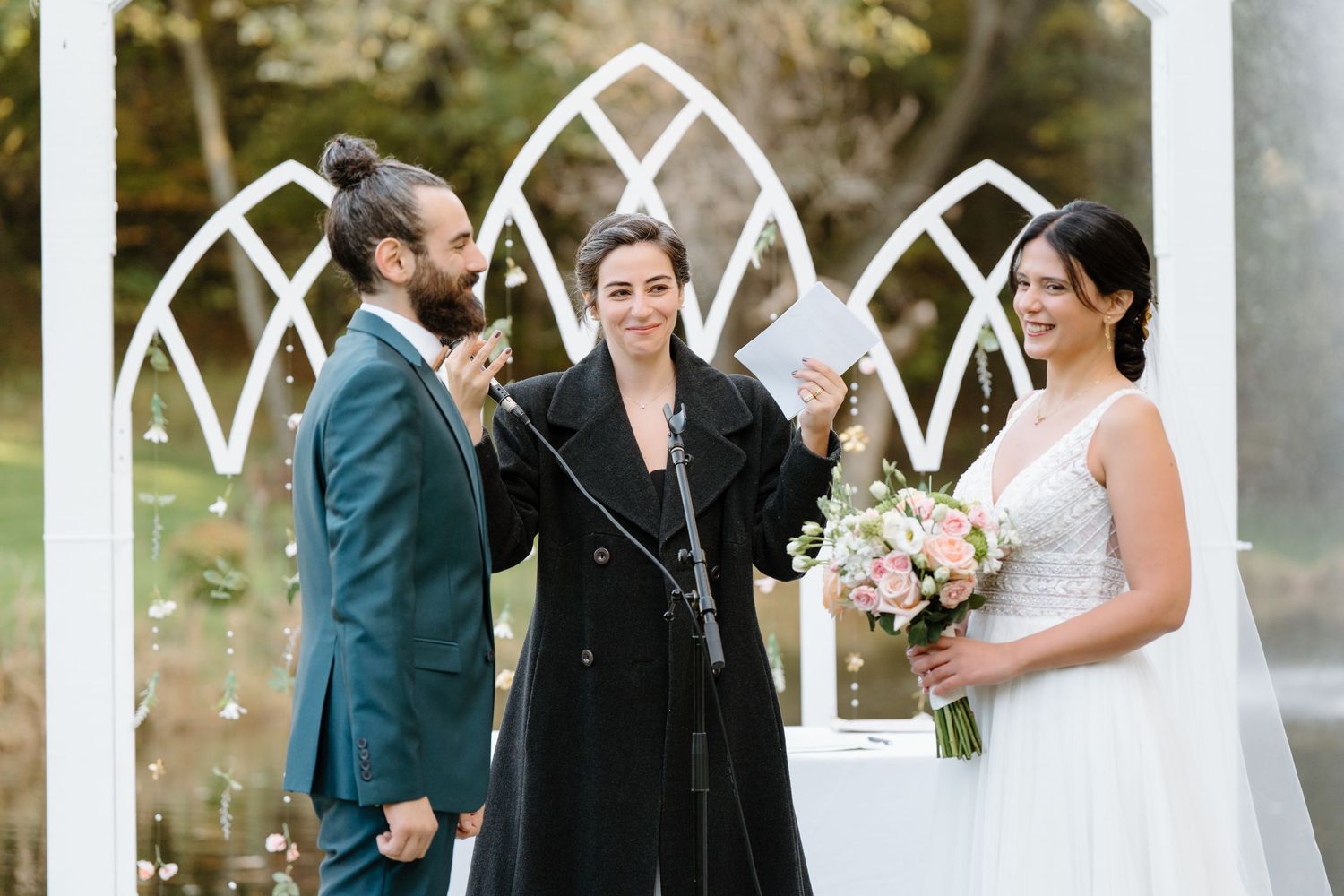 Wedding ceremony under decorative white arch with officiant and couple sharing joyful moment.