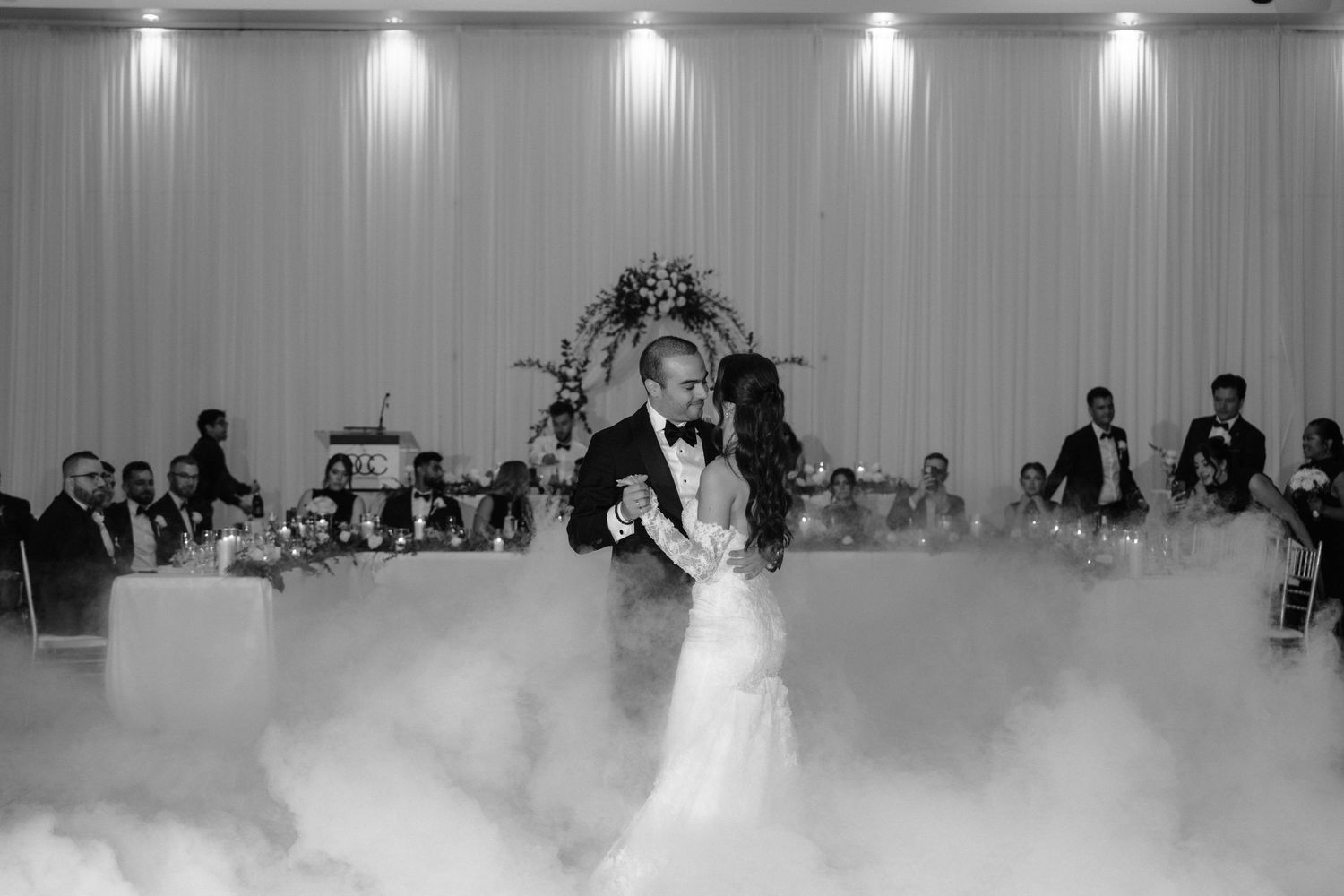 A bride and groom share their first dance at a wedding reception with dramatic fog effects on the dance floor.