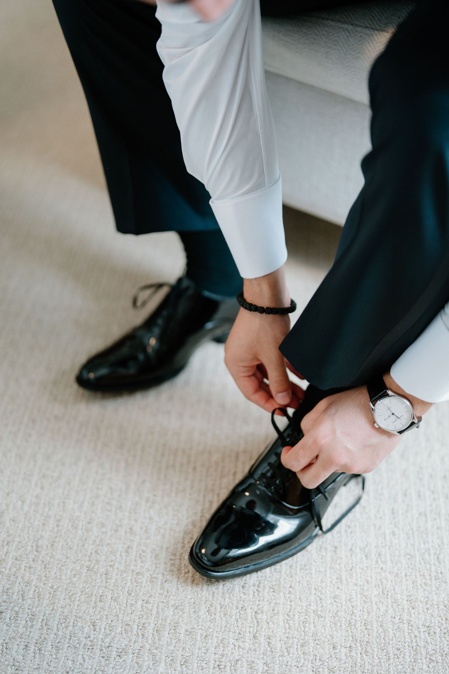 Close-up sequence showing hands adjusting and fastening formal black dress shoes on carpeted floor.