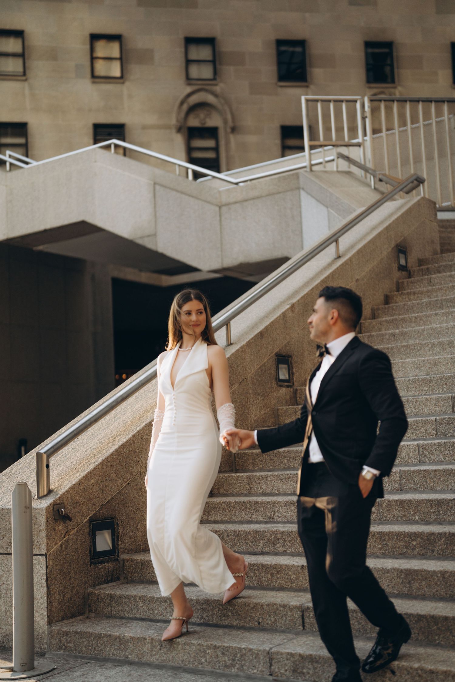 A couple walks down concrete steps together in a romantic sequence of candid wedding portraits.