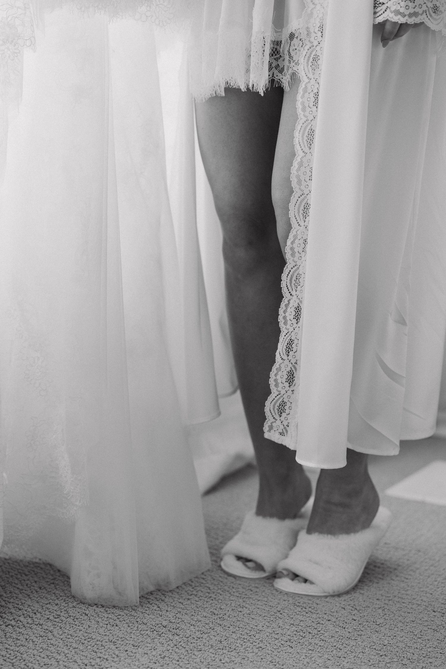 Black and white photograph showing the bottom portion of wedding dresses and feet in a bridal boutique.