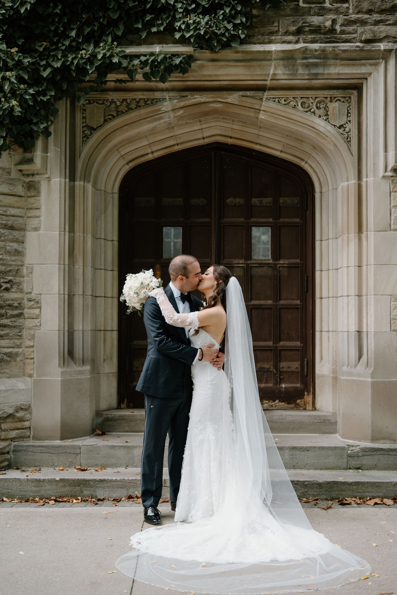 Newlyweds share a tender moment outside a grand stone church entrance with gothic architecture.
