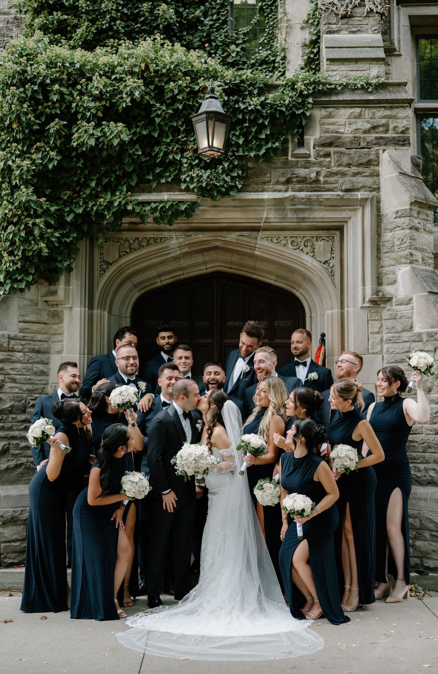 Wedding party in black attire poses playfully in sequence of three photos outside stone building with arched doorway.