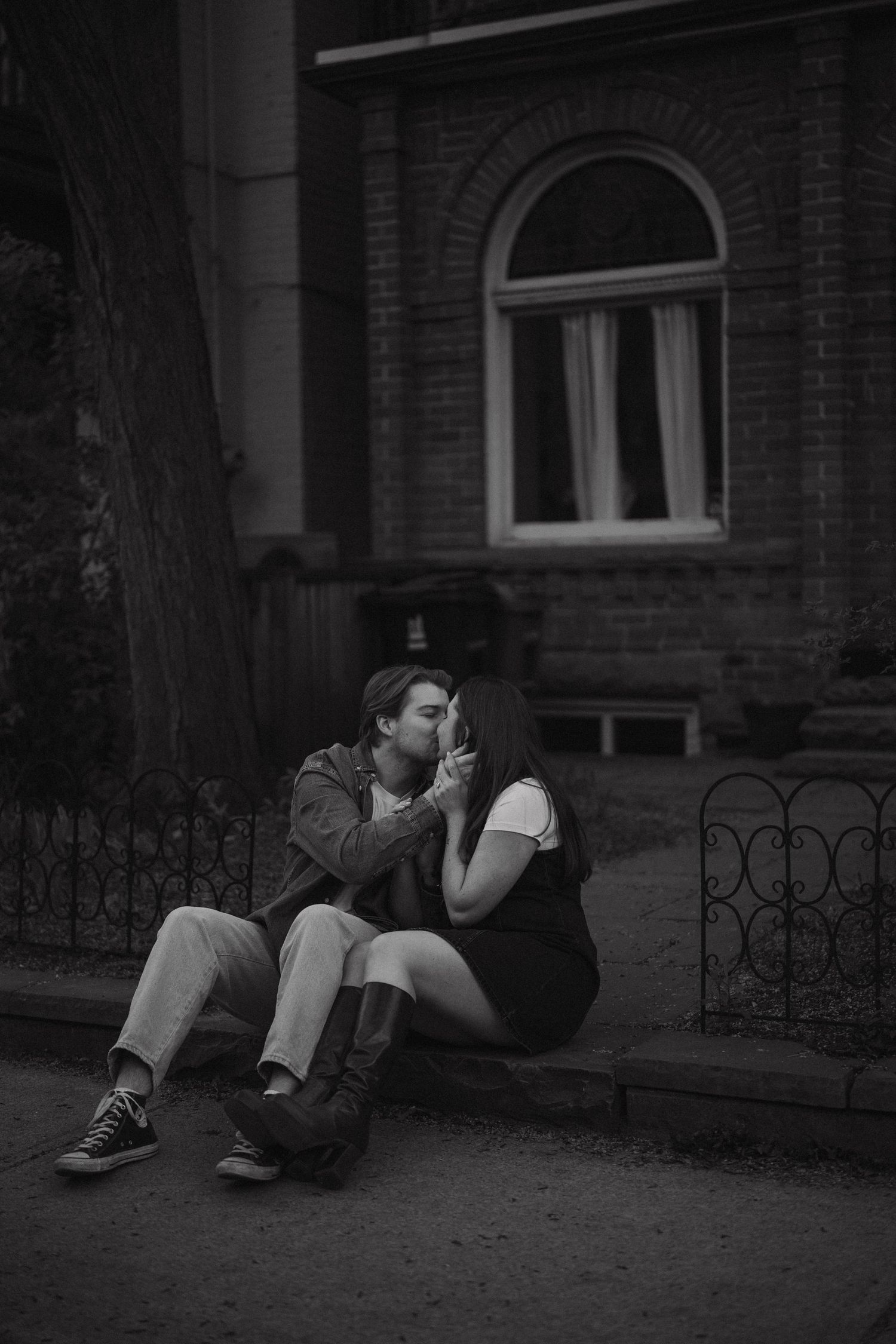 A romantic black and white vintage-style photograph of a couple sitting together on steps in front of a brick building.